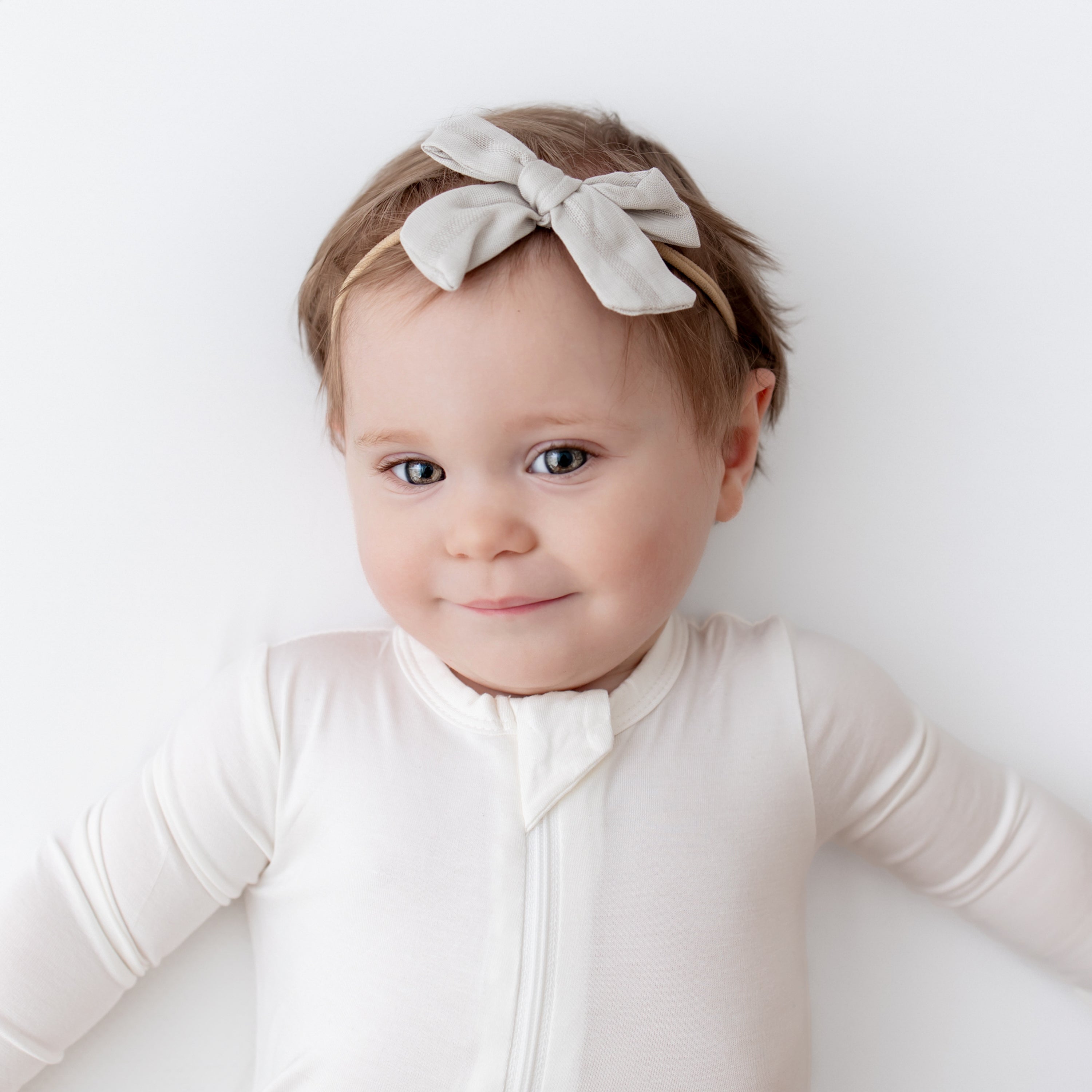 Smiling baby wearing Bamboo Muslin Medium Bow in Oat and matching zippered romper