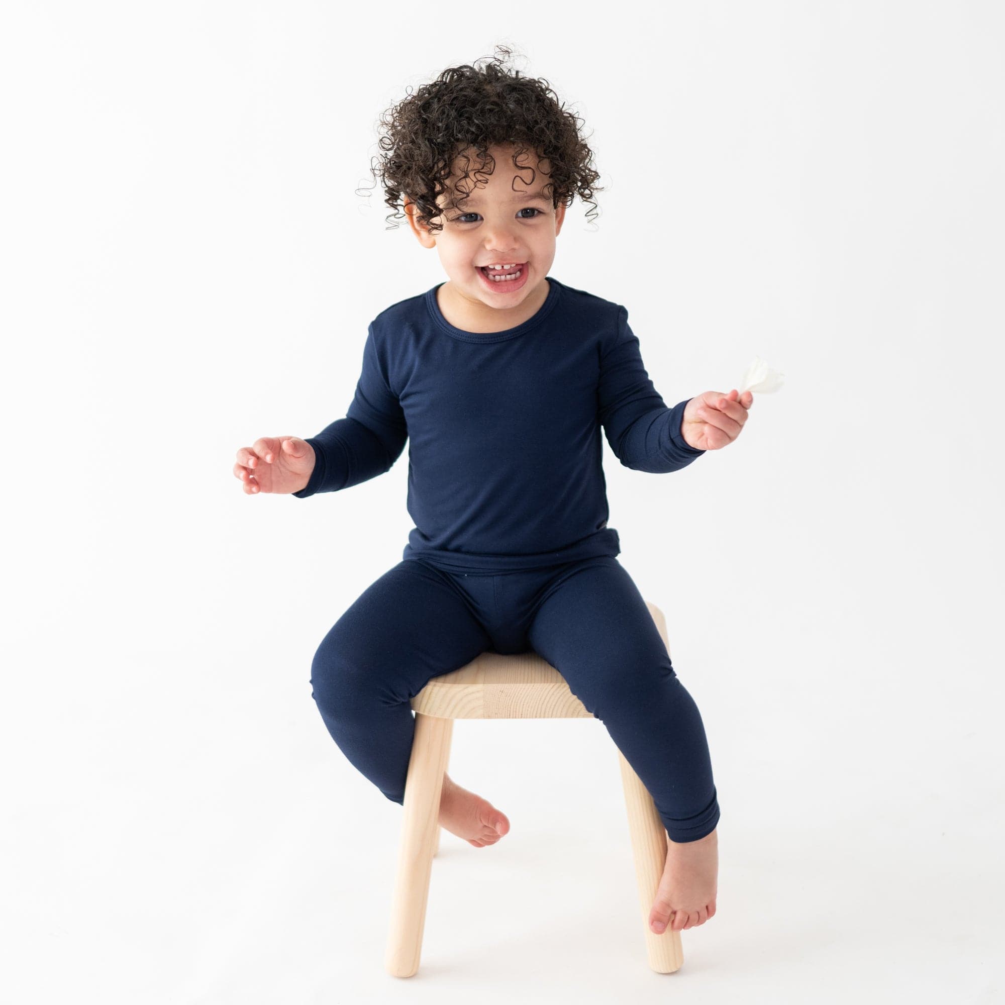 toddler in long sleeve pajamas in navy sitting on a stool