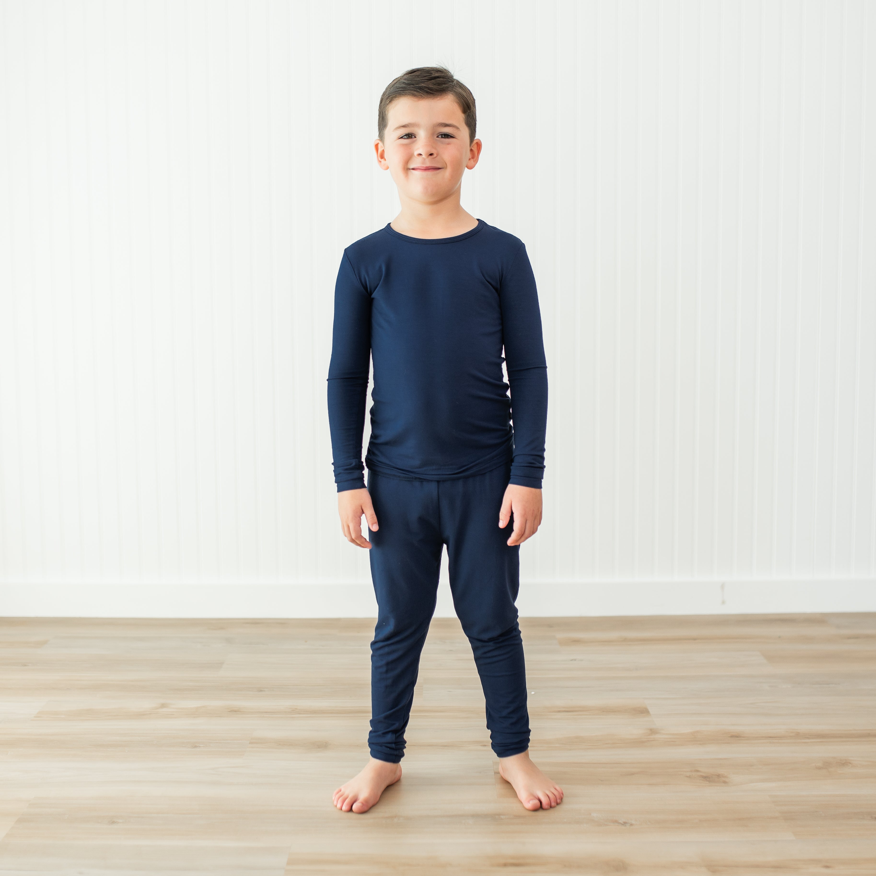 Child wearing a navy blue long-sleeve shirt and pant pajama set on a light wooden floor.