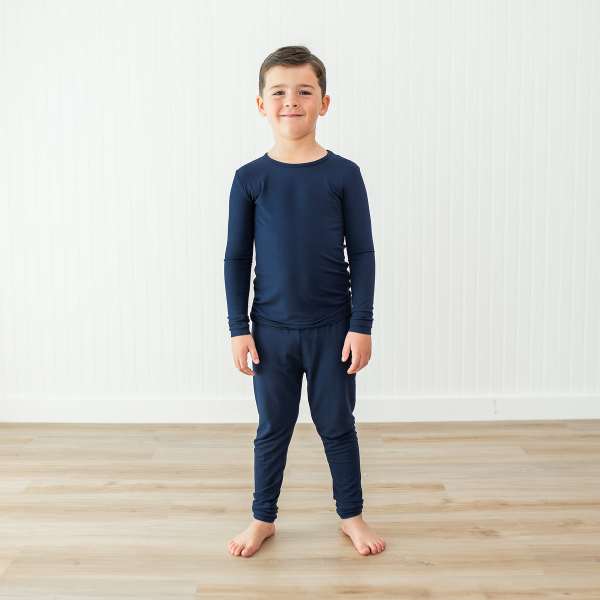 Child wearing a navy blue long-sleeve shirt and pant pajama set on a light wooden floor.