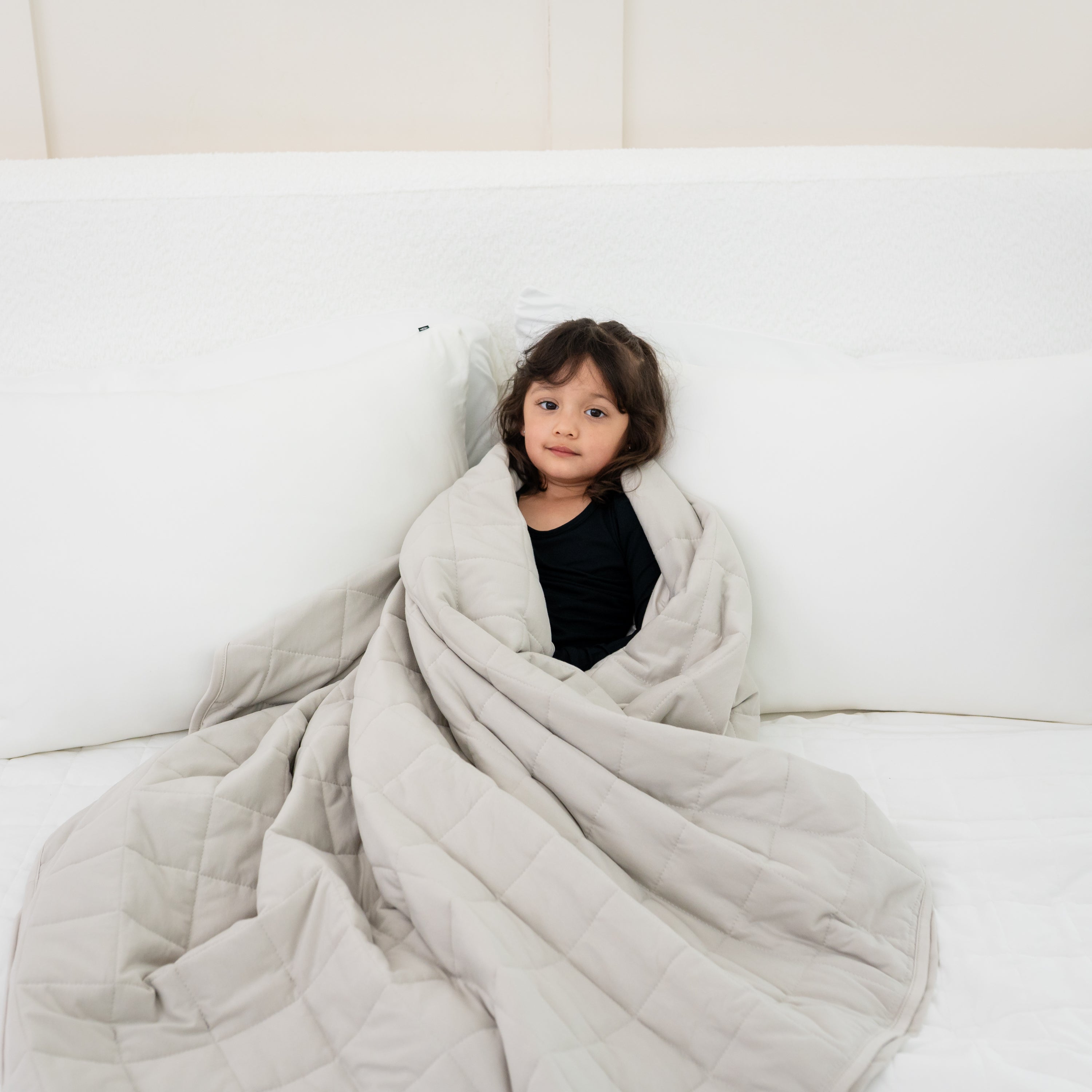 Toddler laying in bed wrapped in Youth Blanket in Oat