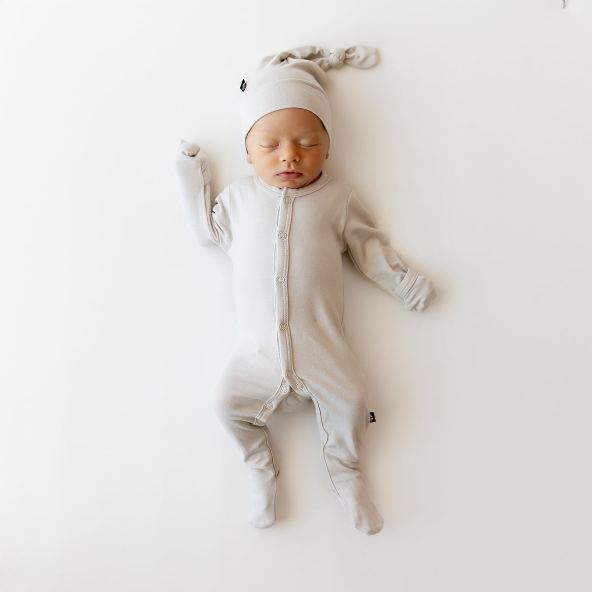 Baby in a snap footie in a creamy light grey with matching knotted cap