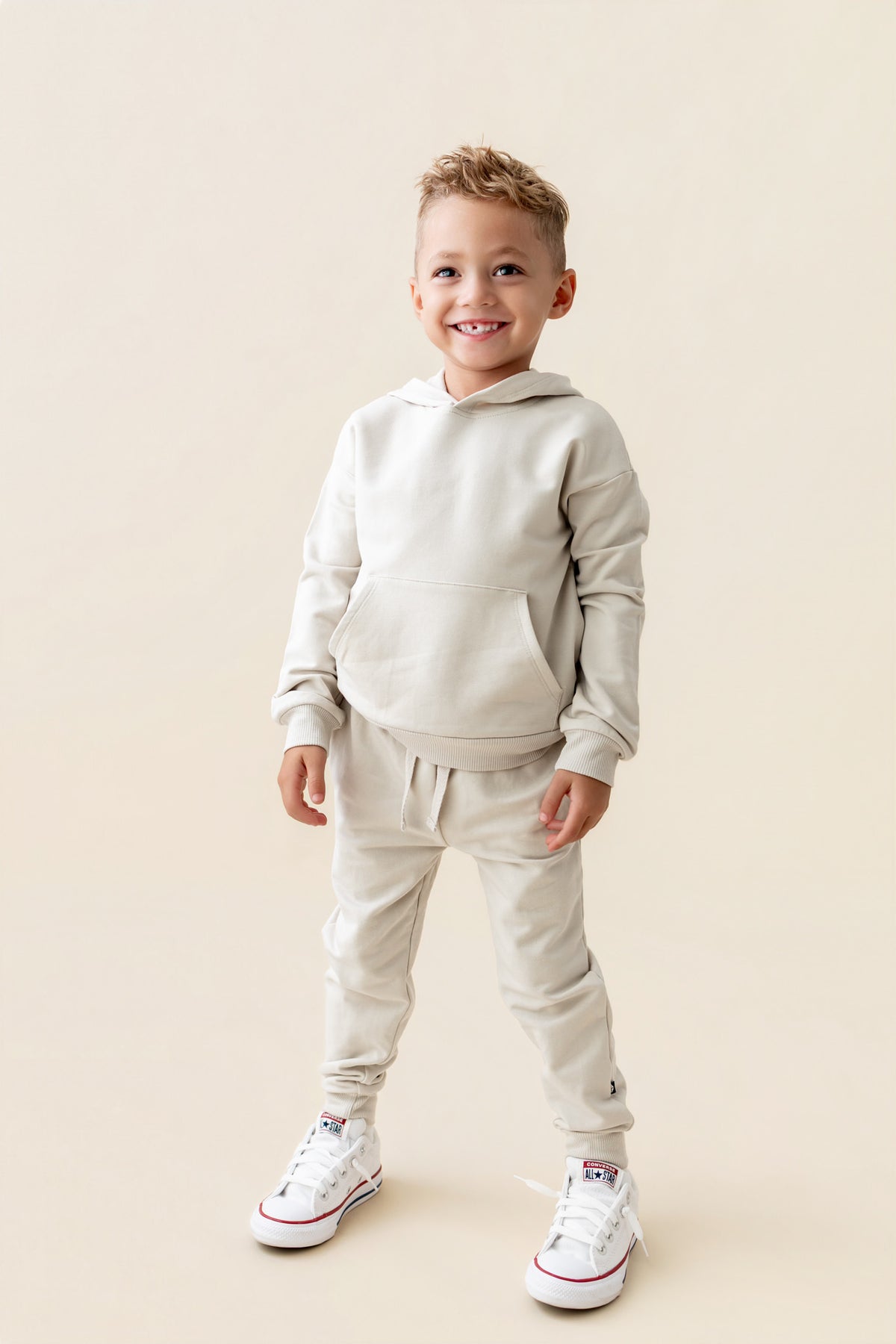 Boy posing in Hoodie in Oat color over similar color jogger pants on a beige background