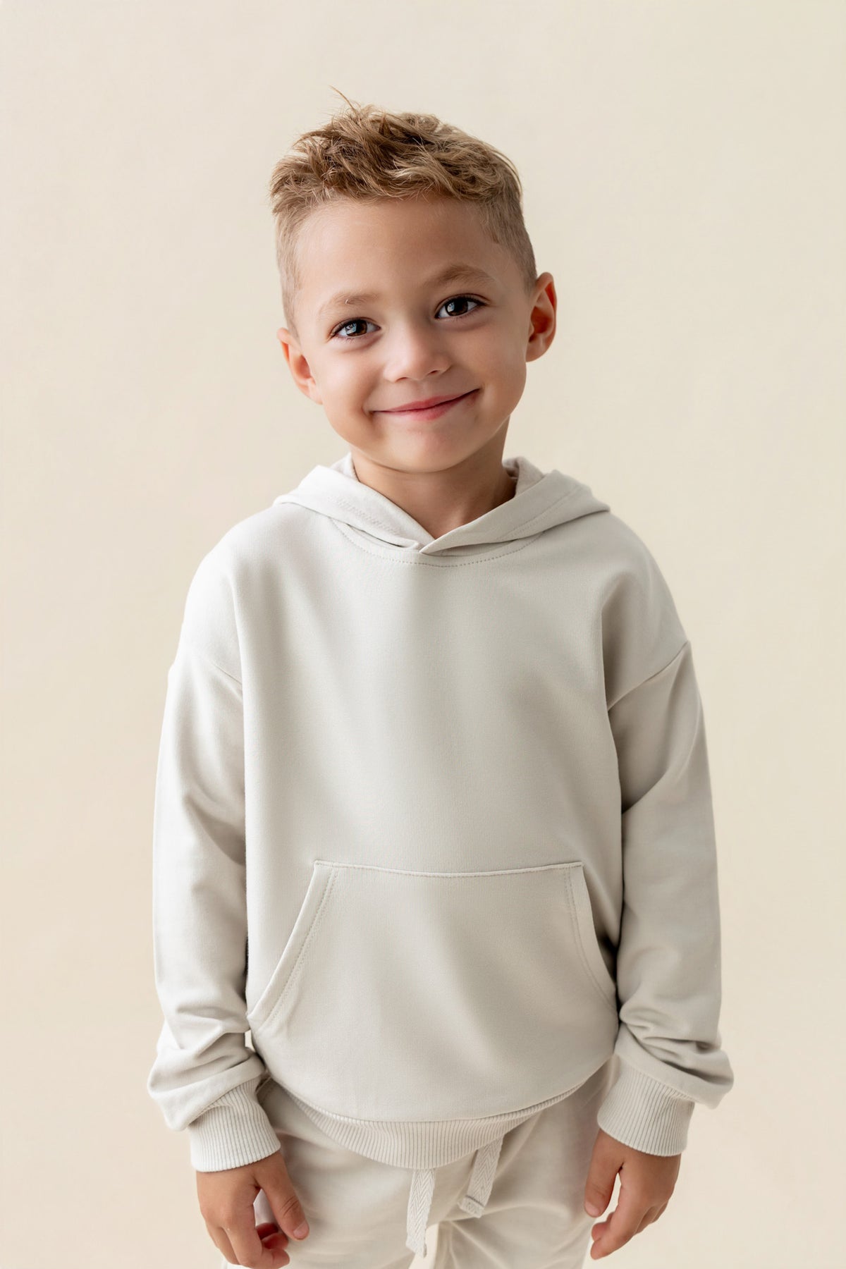 Boy smiling in Hoodie in Oat color on a beige background
