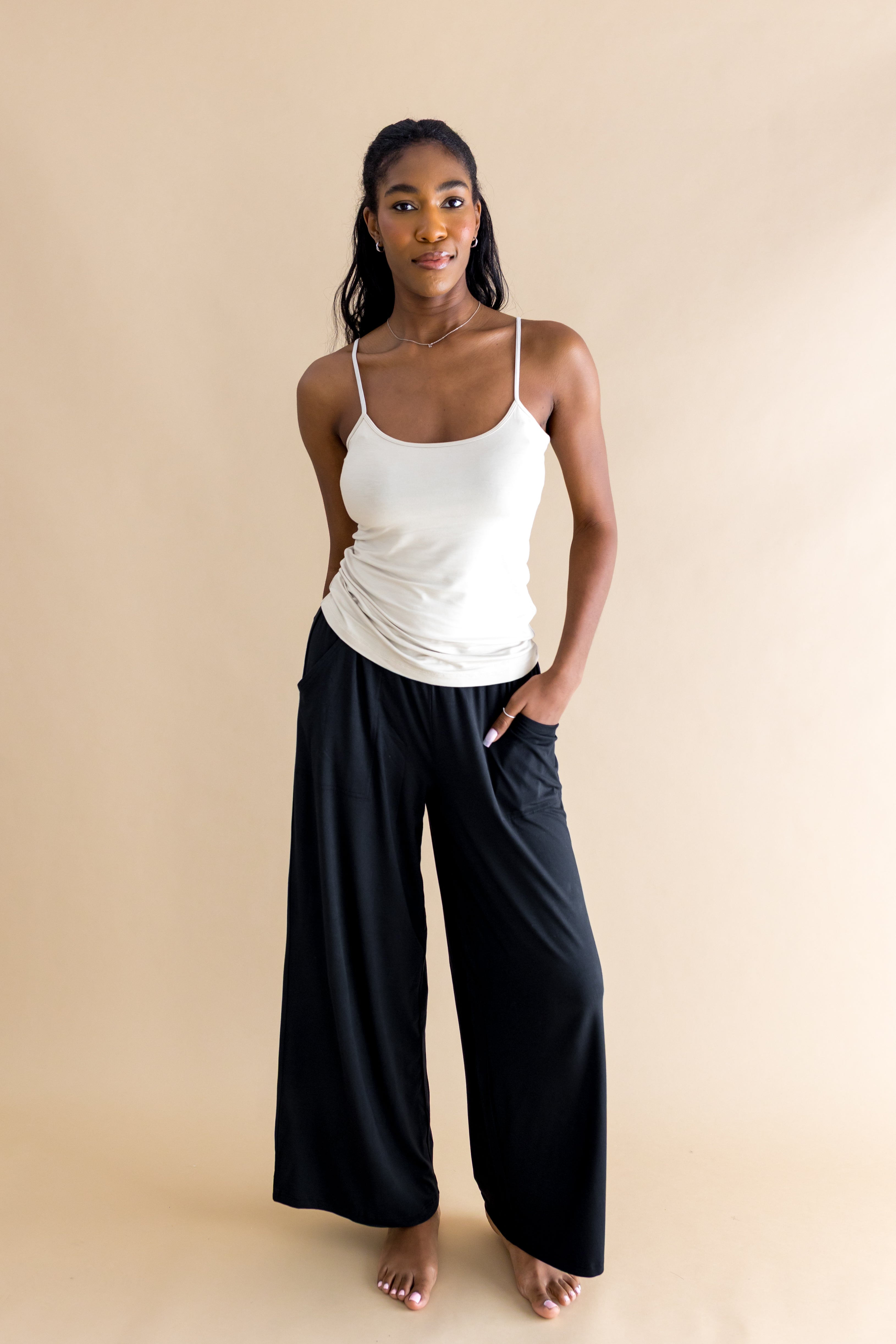 Woman wearing a off white tank top and black wide-leg pants on a beige background