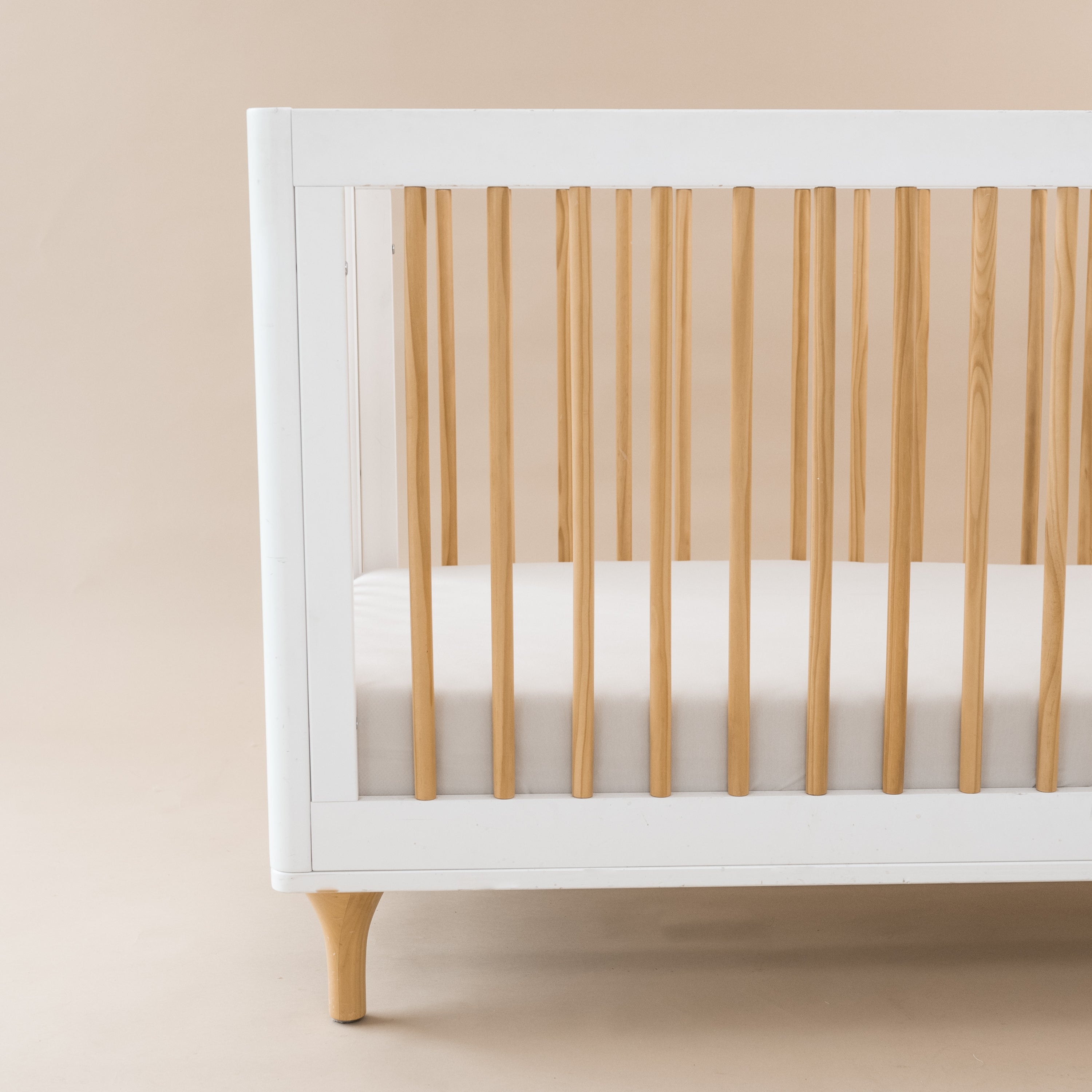 Crib Sheet in Oat shown on a mattress in a modern white and wooden crib