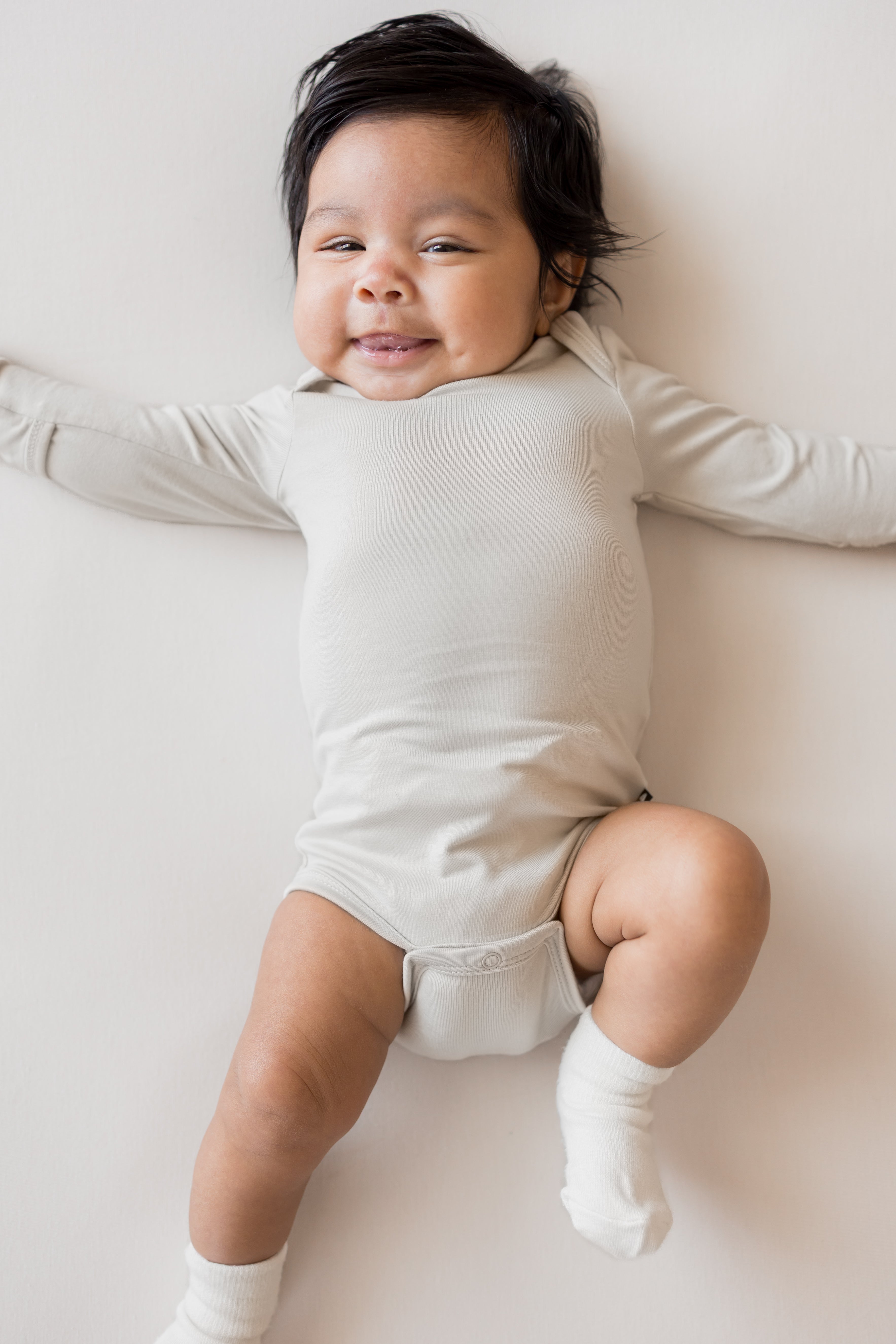 Close up of Baby wearing Long Sleeve Bodysuit in Oat color and white socks on a beige background