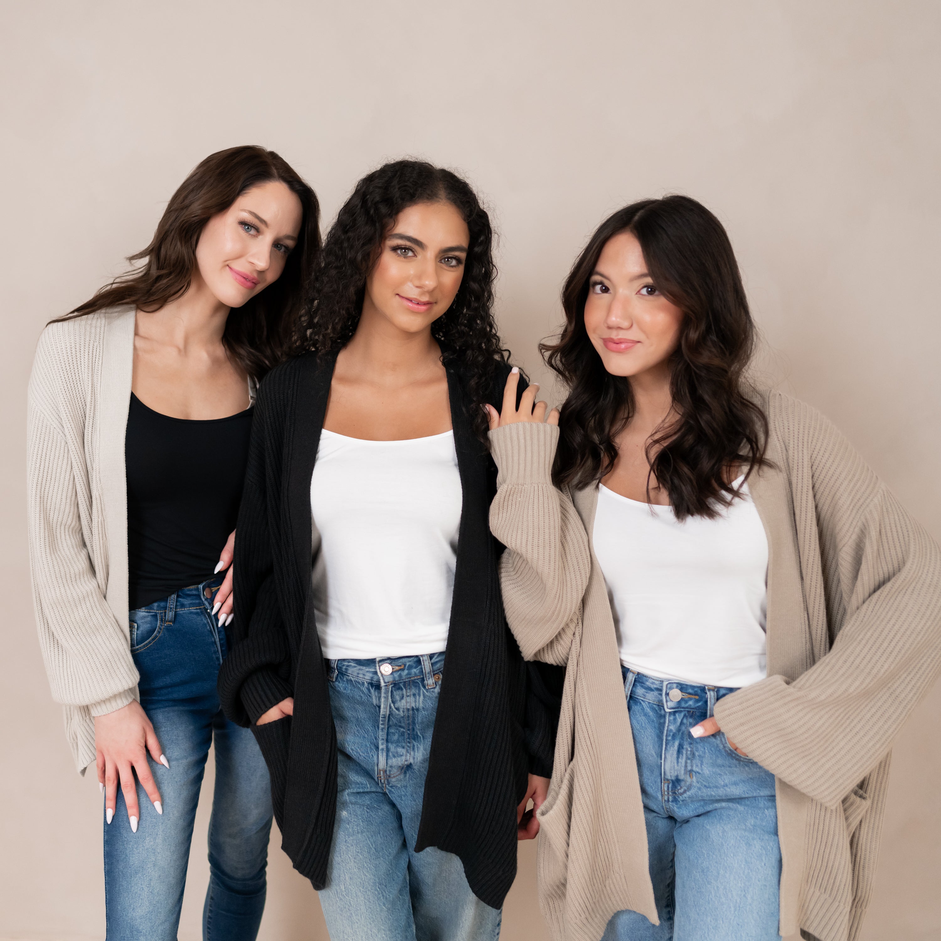 Three models standing side by side wearing the Chunky Knit Women's Oversized Cardigan in Almond, Midnight and Oat