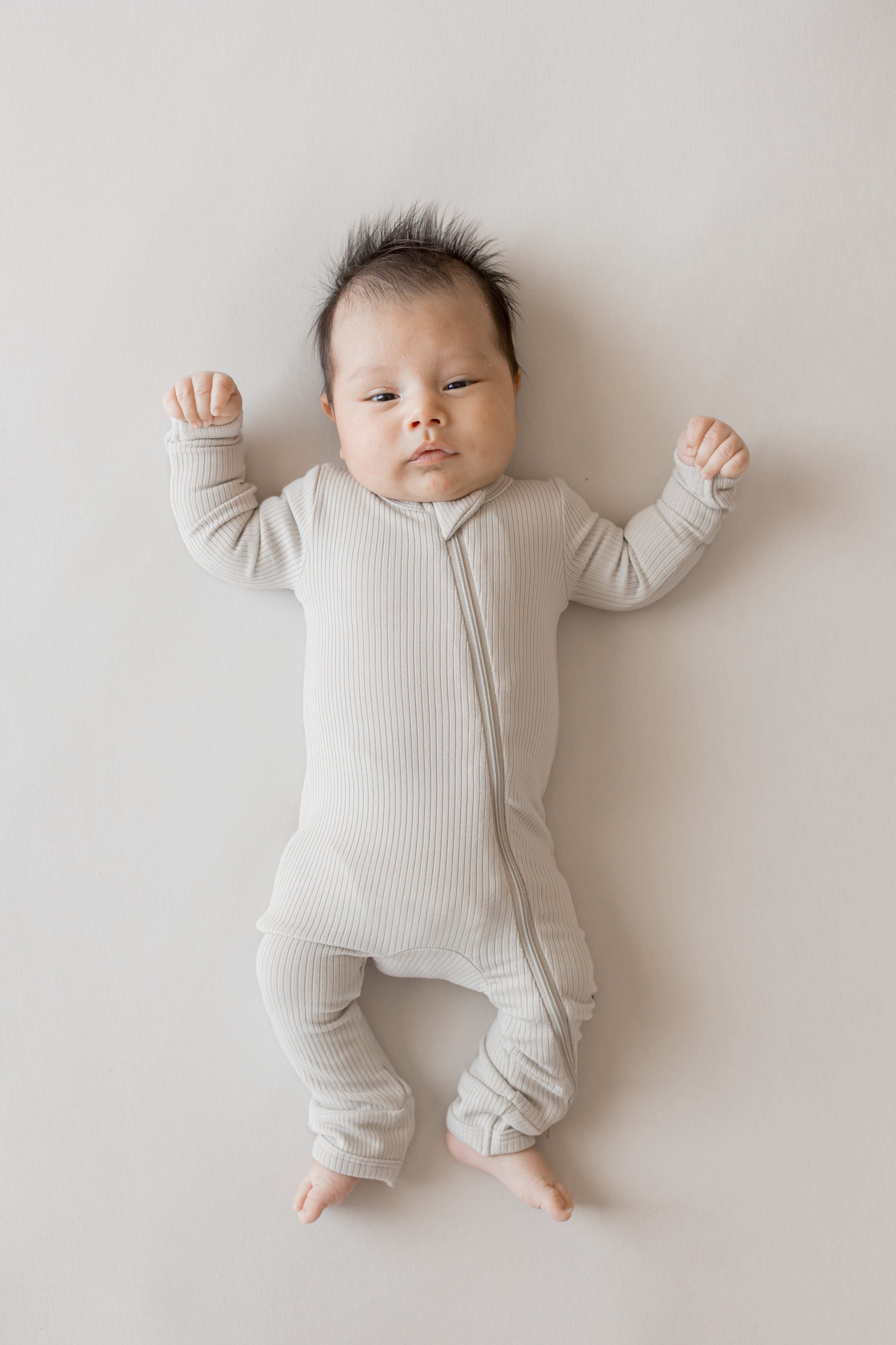 Baby wearing Ribbed Zipper Romper in Oat color on a beige background