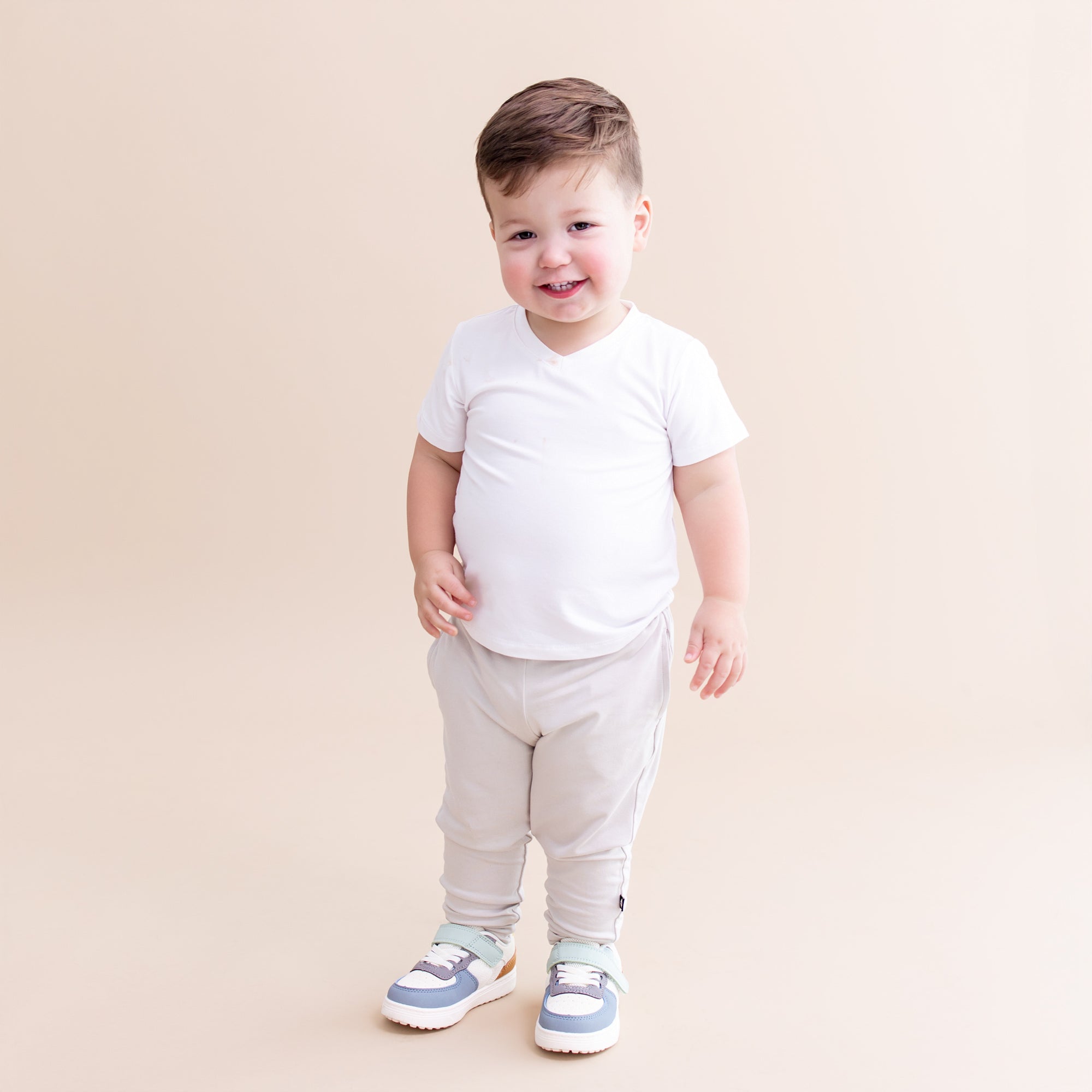 Young toddler model wearing the Toddler Jogger Pant in Oat with a white v-neck short sleeve shirt