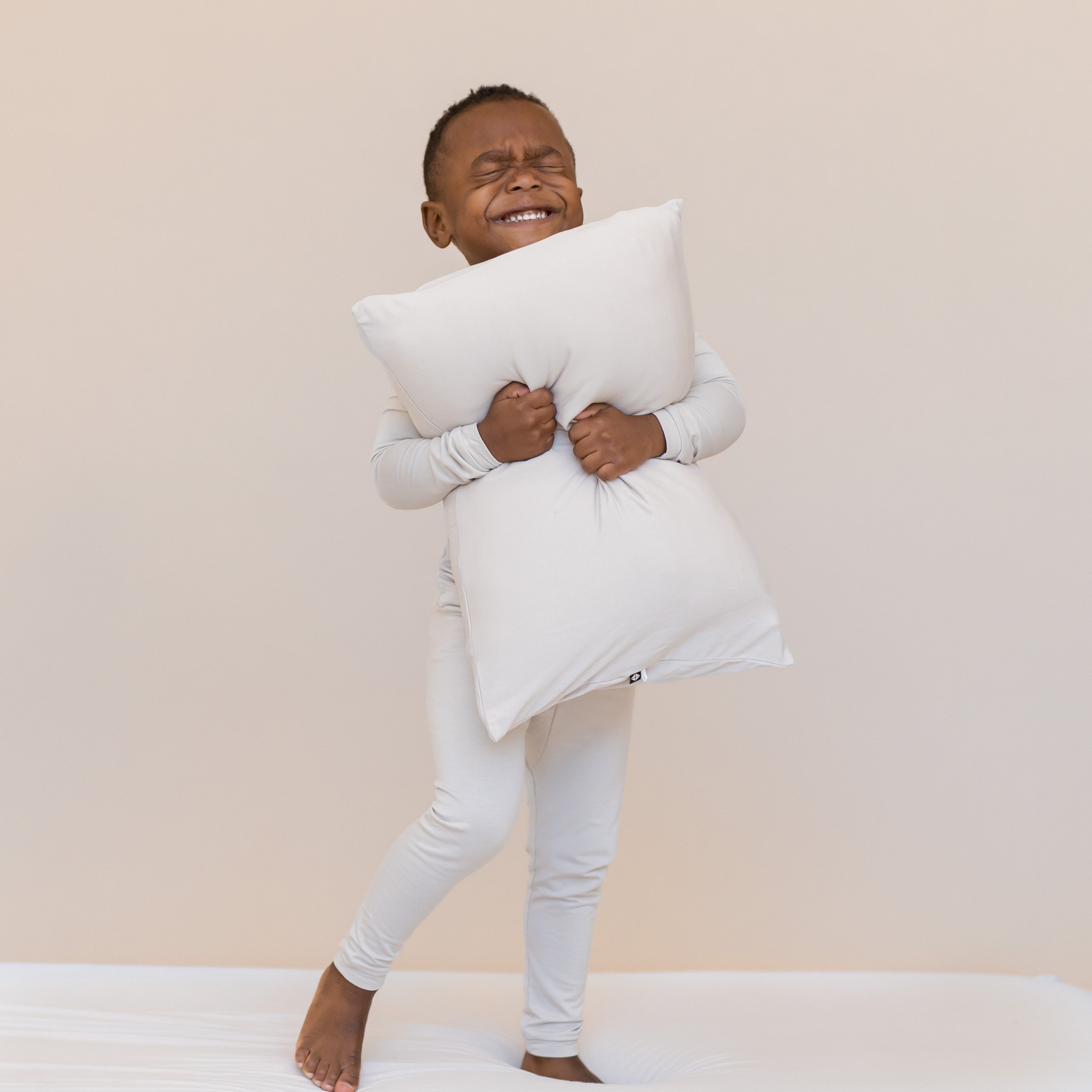 Young boy wearing an off-white long sleeve pajama set snuggling a pillow