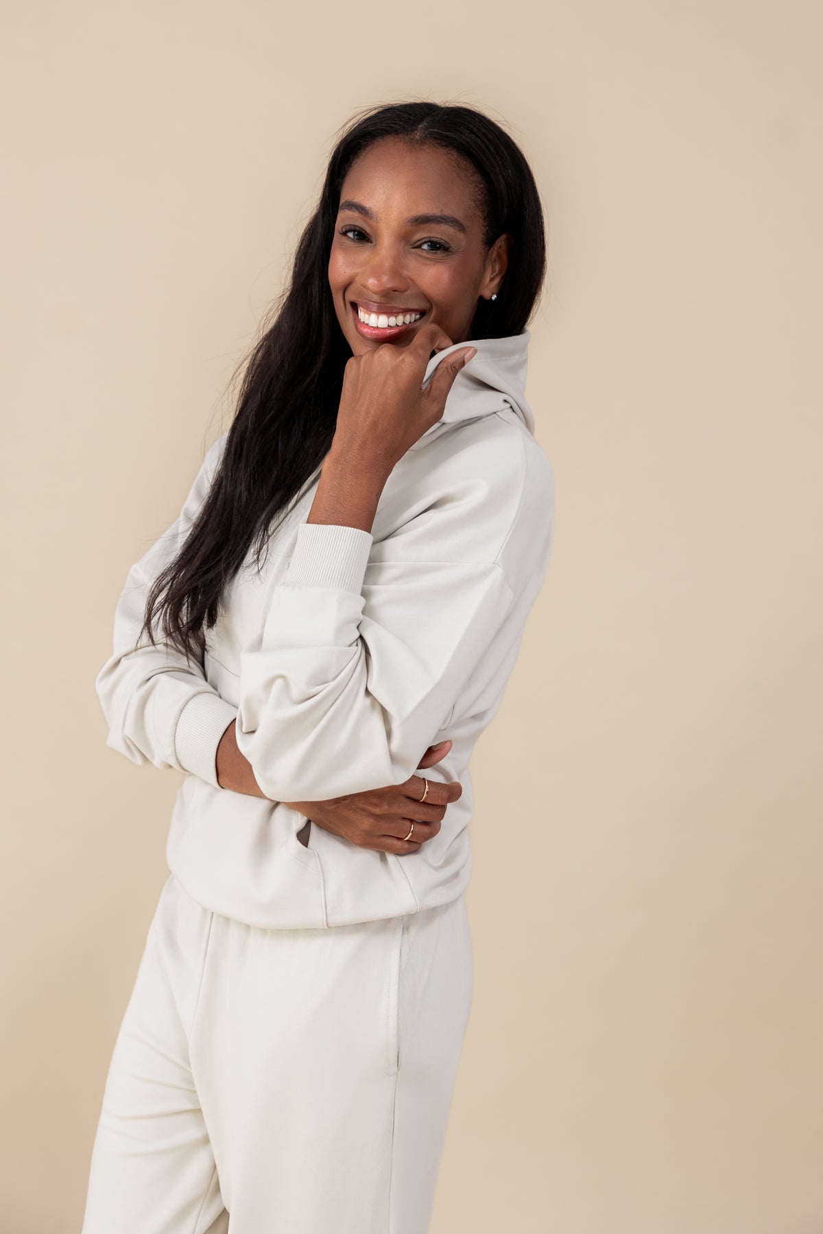 Modal smiling wearing Women's Hoodie in Oat color over similar color jogger pants on a beige background