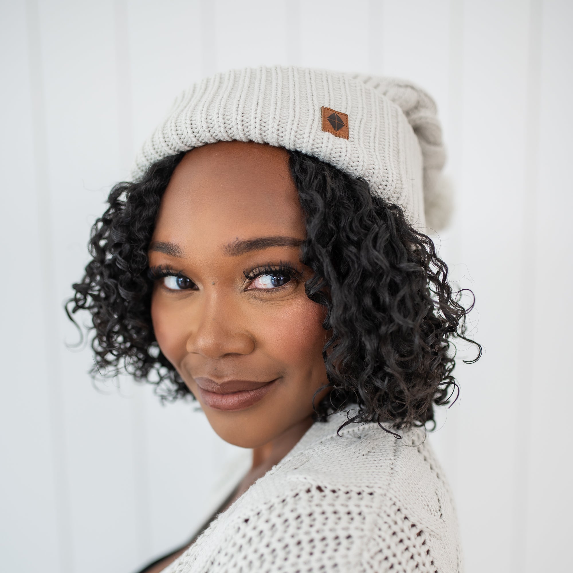 Close up of a female model wearing the Cable Knit Adult Pom Beanie in Oat