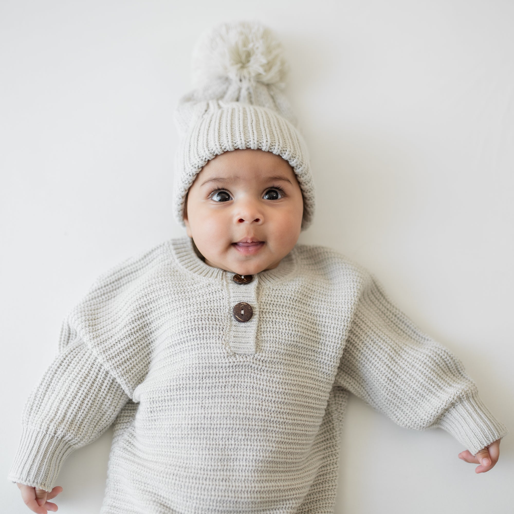 Infant lying down wearing the Chunky Cable Knit Beanie in Oat