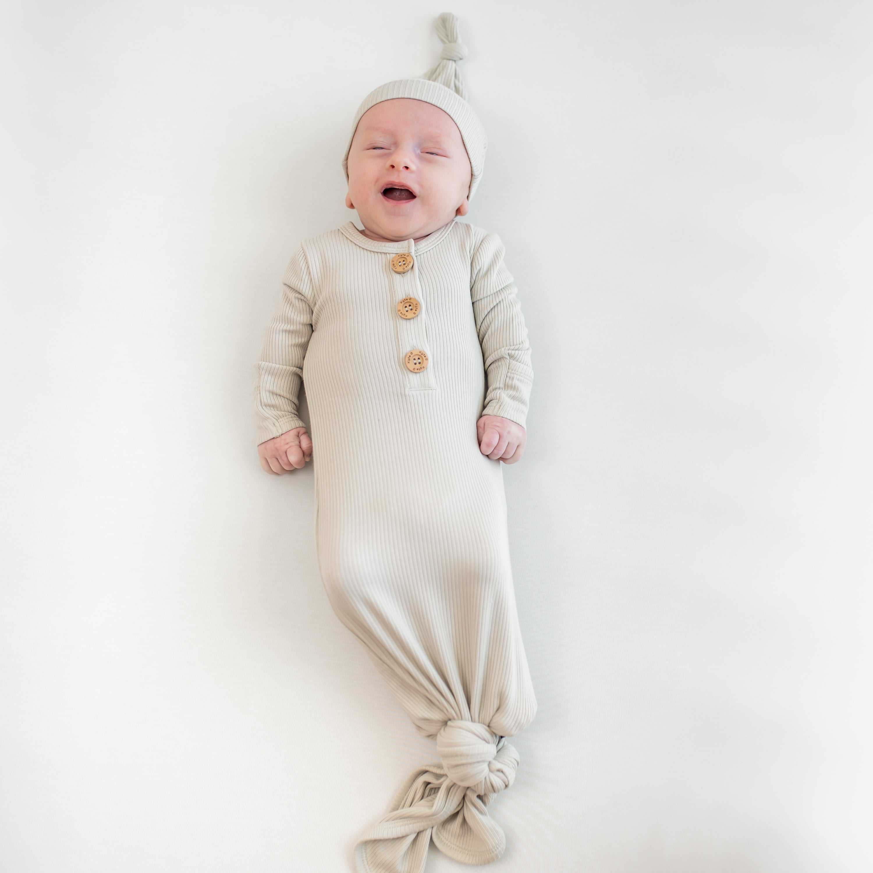 Baby wearing in a beige ribbed gown with buttons on a white background