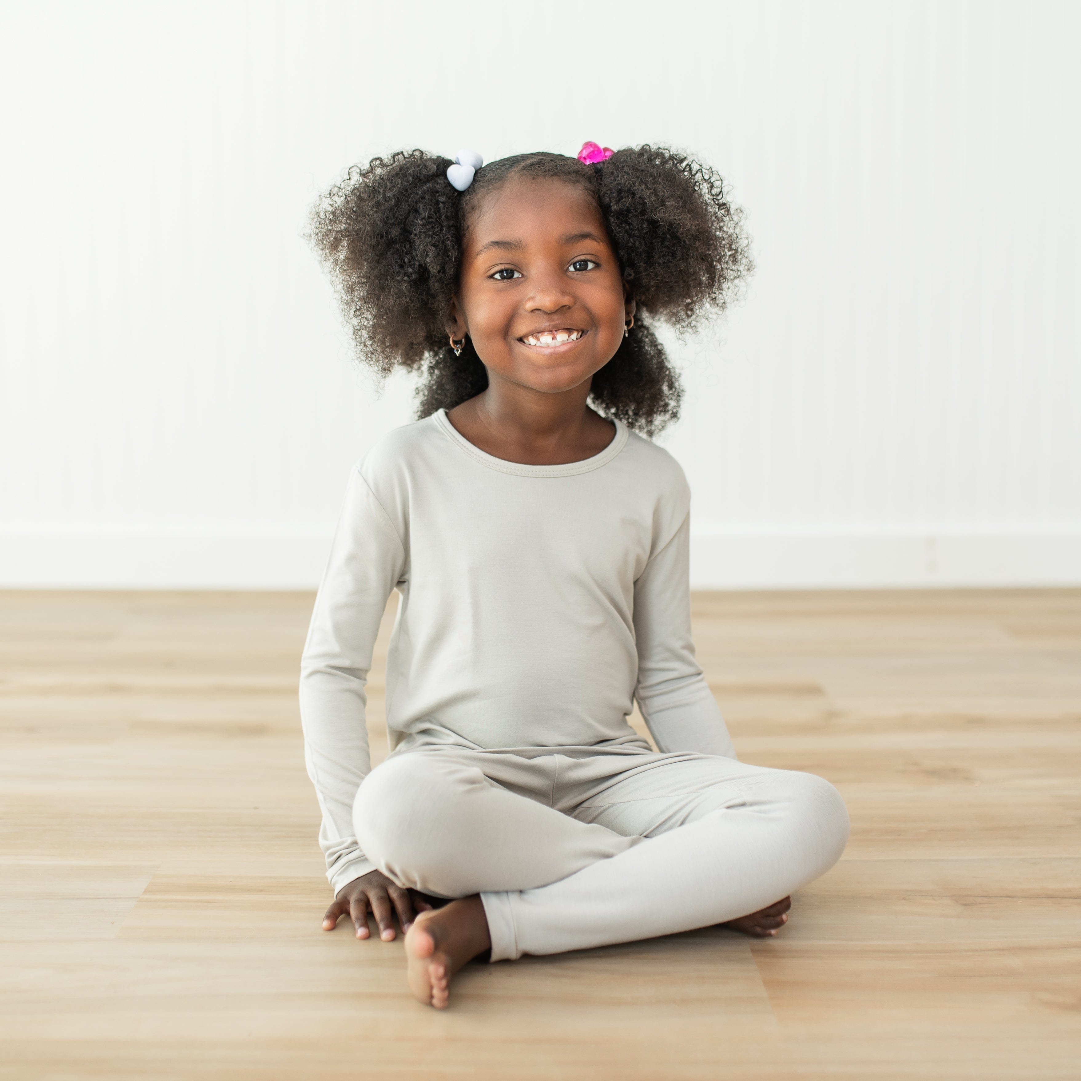 Girl wearing creamy light grey colored long sleeve pajamas sitting on a wooden floor