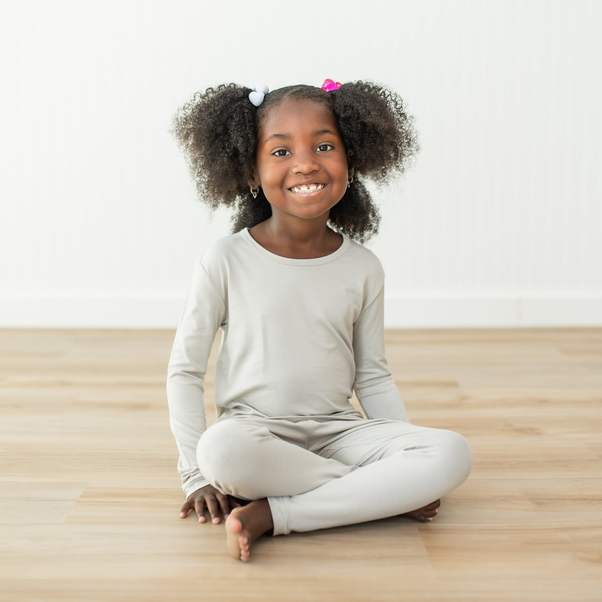 Girl wearing creamy light grey colored long sleeve pajamas sitting on a wooden floor