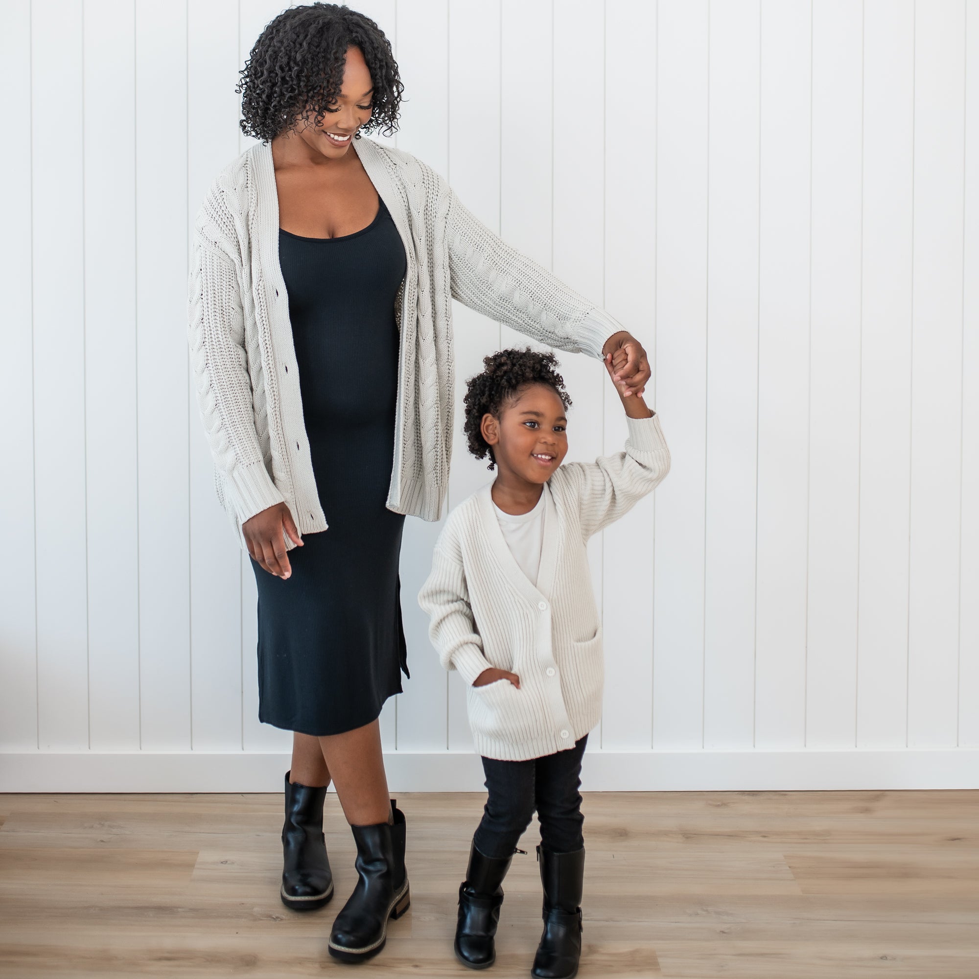 Mother wearing the Cable Knit Cardigan in Oat twirling her daughter who is wearing the Chunky Knit Oversized Cardigan in Oat