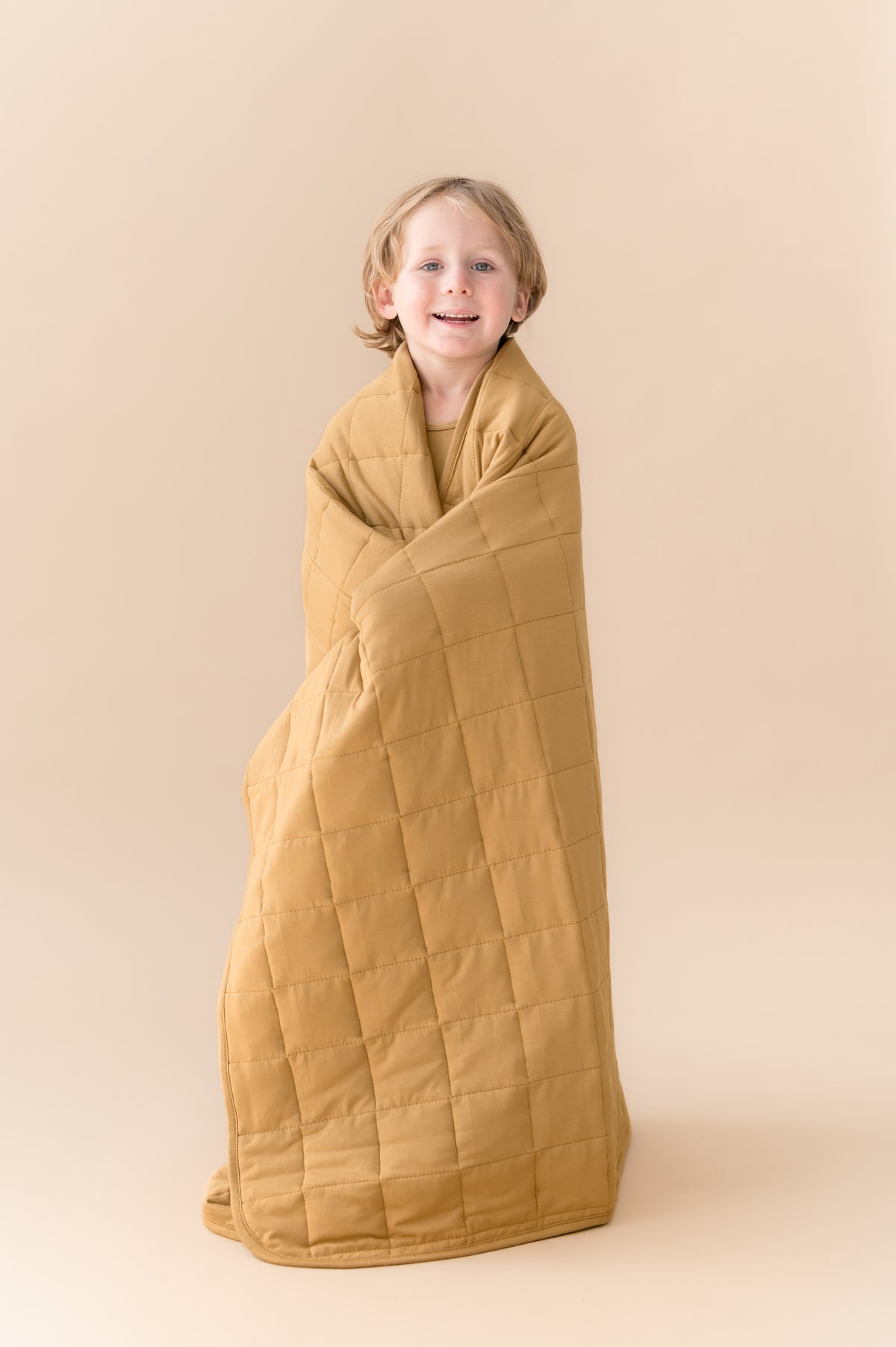 Child wrapped in Toddler Blanket in Ochre 2.5 on a beige background