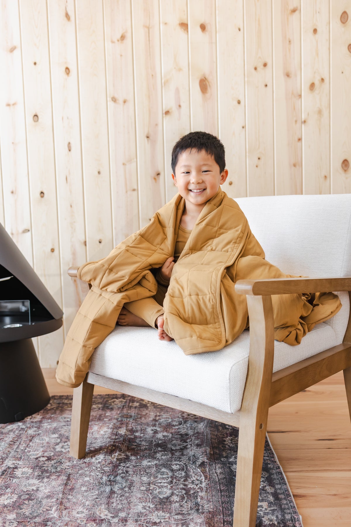 Child covered with Youth Blanket in Ochre 2.5 sitting on a white chair