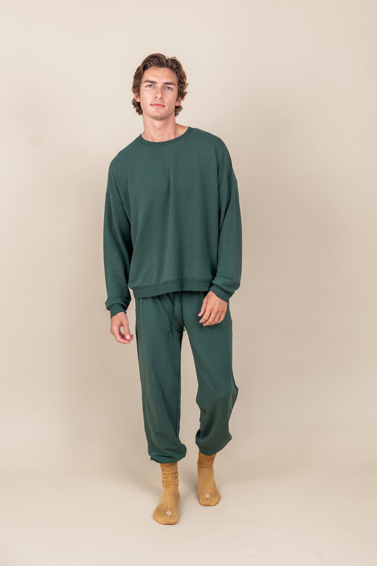 Modal wearing Adult Scrunch Socks in Ochre color while wearing green jogger set on a beige background