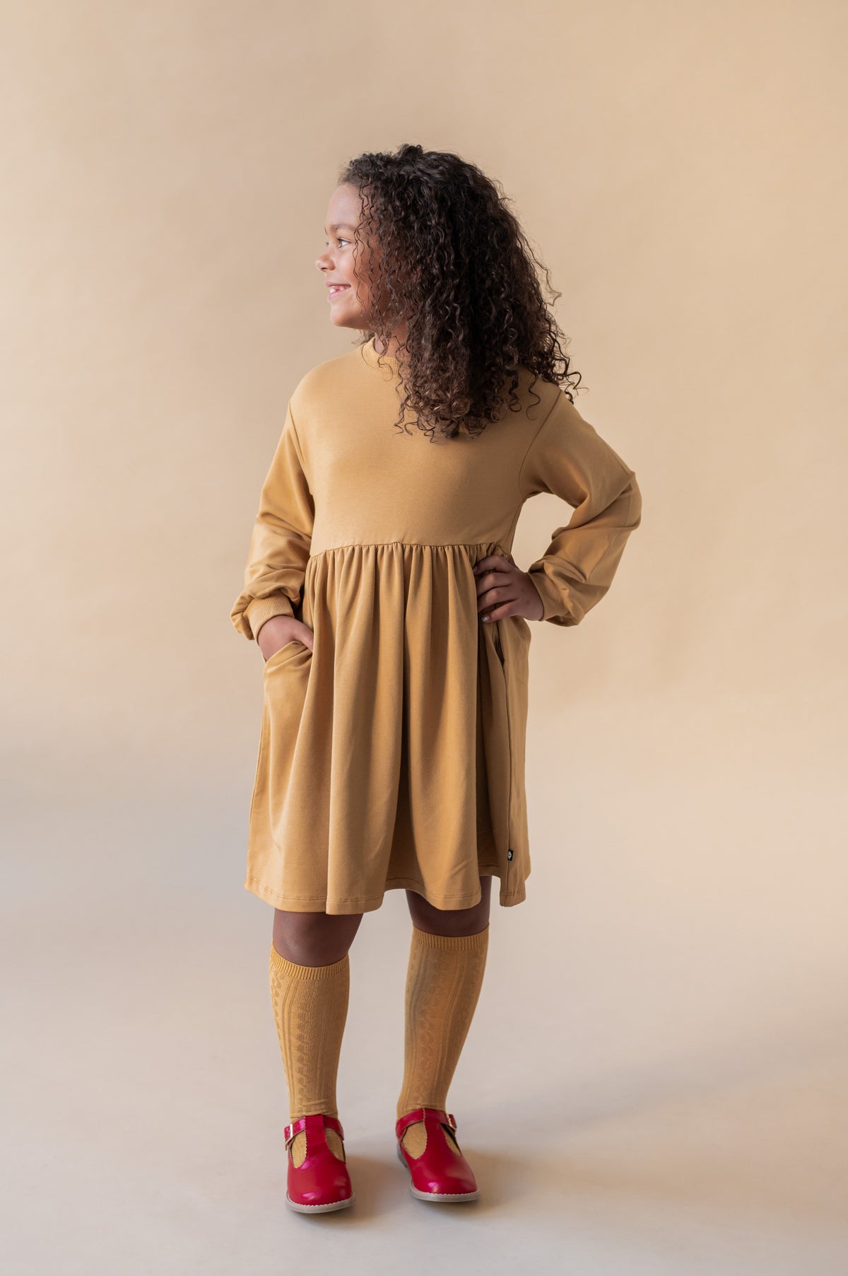 Girl posing in Long Sleeve Skater Dress in Ochre color on a beige background