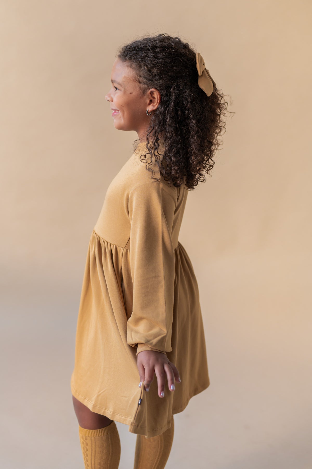 Side pose of Girl wearing Long Sleeve Skater Dress in Ochre color on a beige background