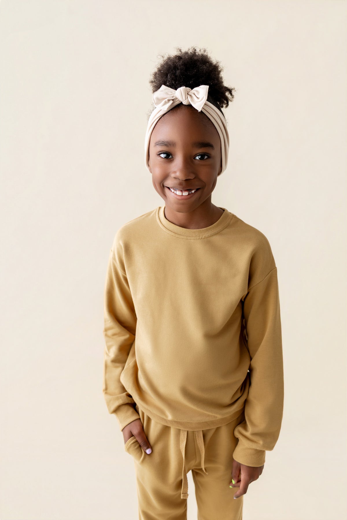 Girl smiling wearing Sweatshirt in Ochre color over similar color jogger pant on a beige background