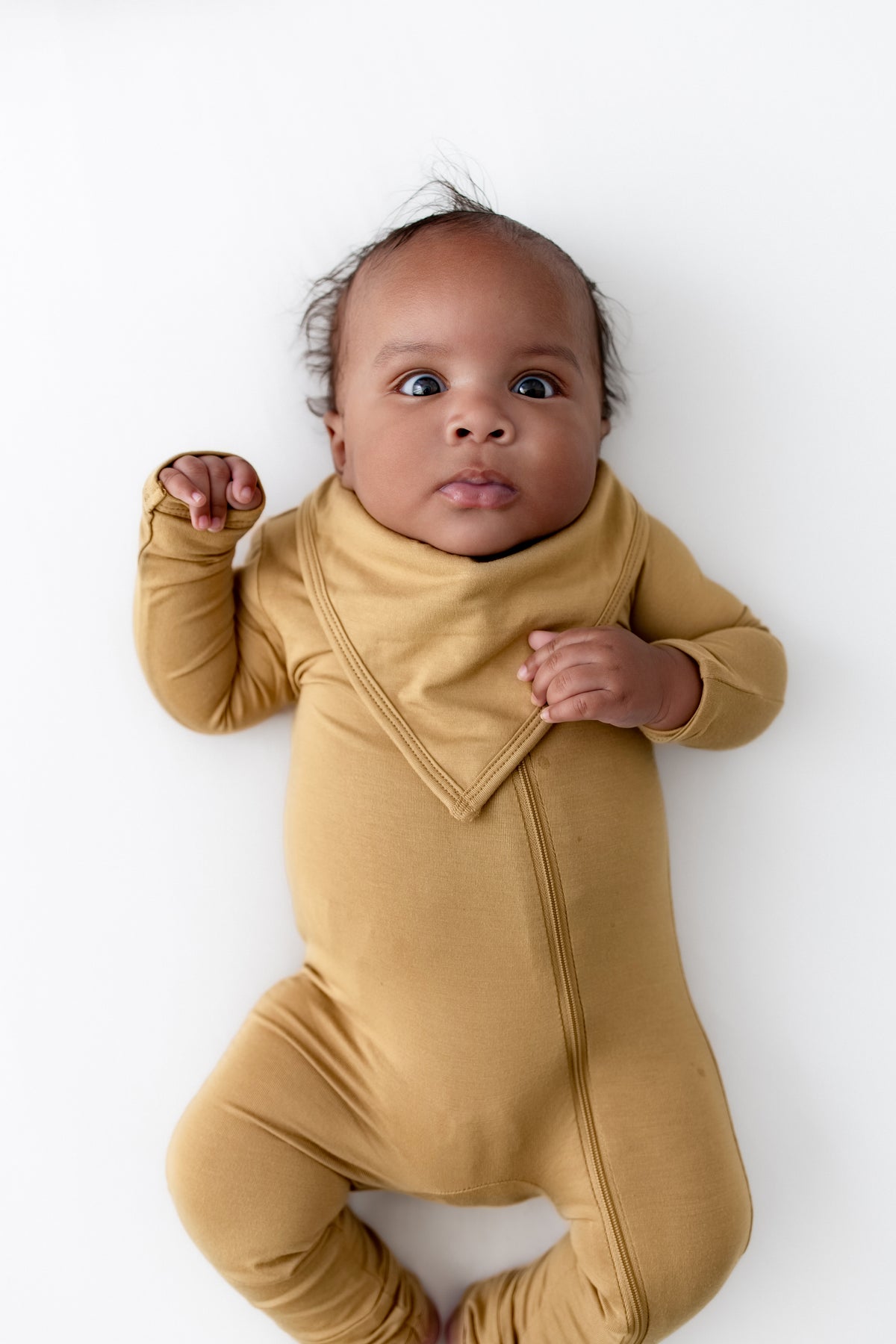 Baby wearing Bib in Ochre over zippered romper in Ochre on a white background