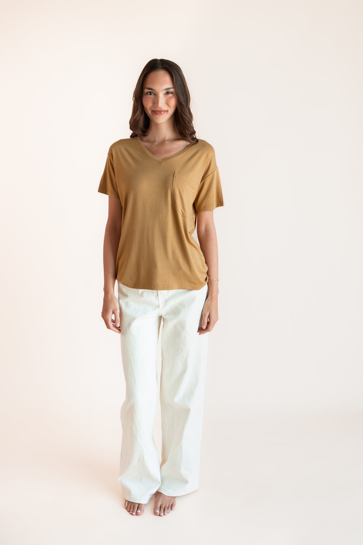 Model posing in Women's Oversized V-Neck Tee in Ochre over white pants on a beige background