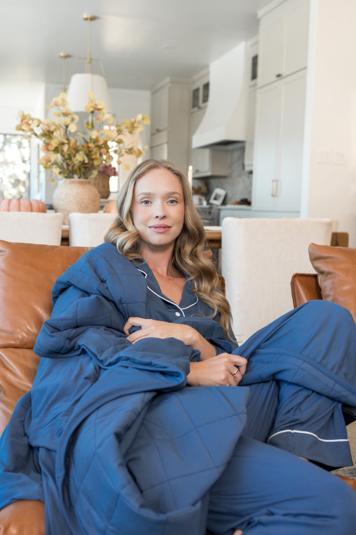 Model wrapped in Adult Quilted Blanket in Oxford 2.5 wearing similar color long sleeve women's pajama set sitting on a couch