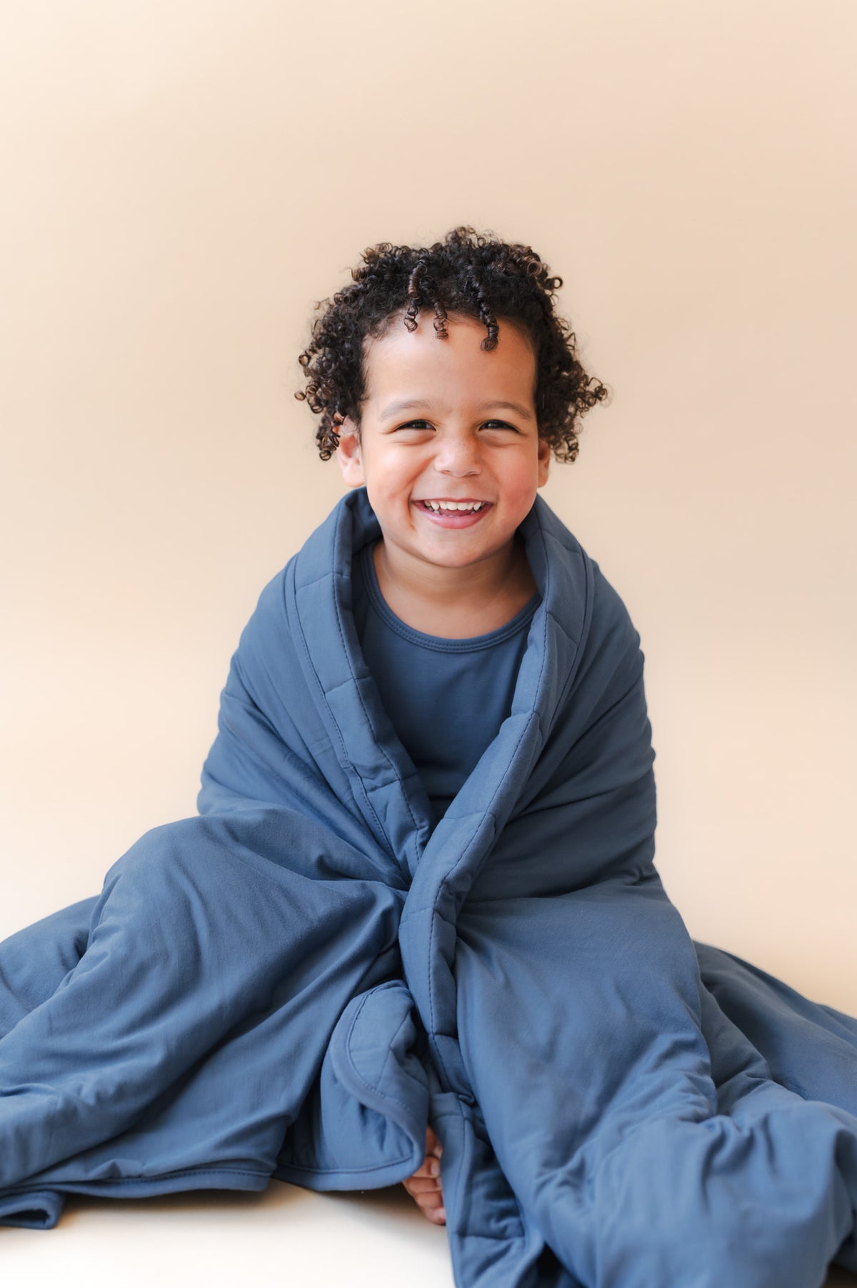Boy sitting with Youth Blanket in Oxford 2.5 wrapped around him over the shoulders on a beige background