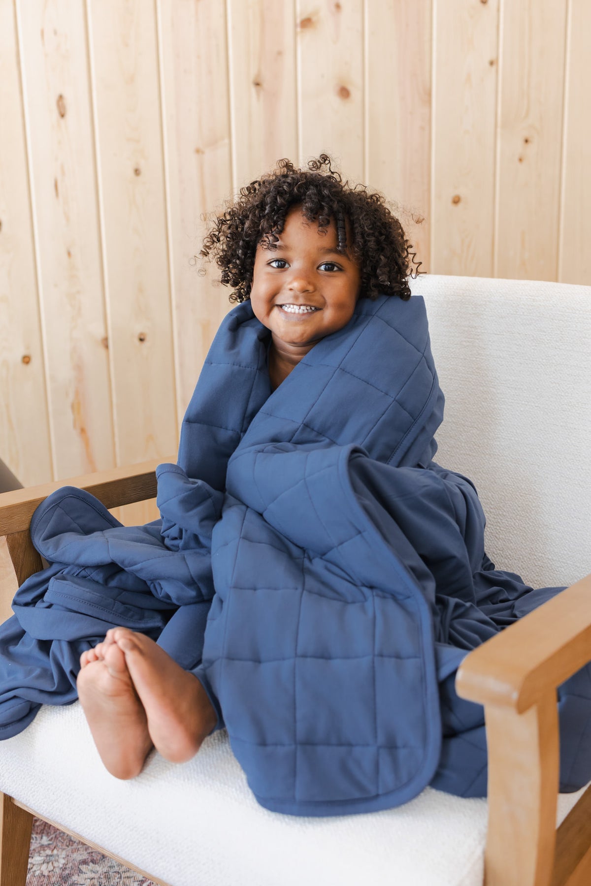 Boy wrapped in Youth Blanket in Oxford 2.5 sitting on a white sofa in a room