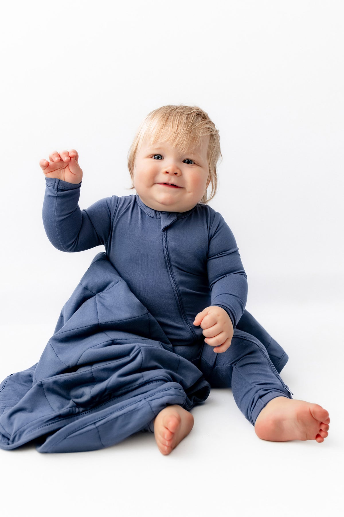 Baby sitting with Baby Blanket in Oxford wearing a similar color zippered romper on a white background