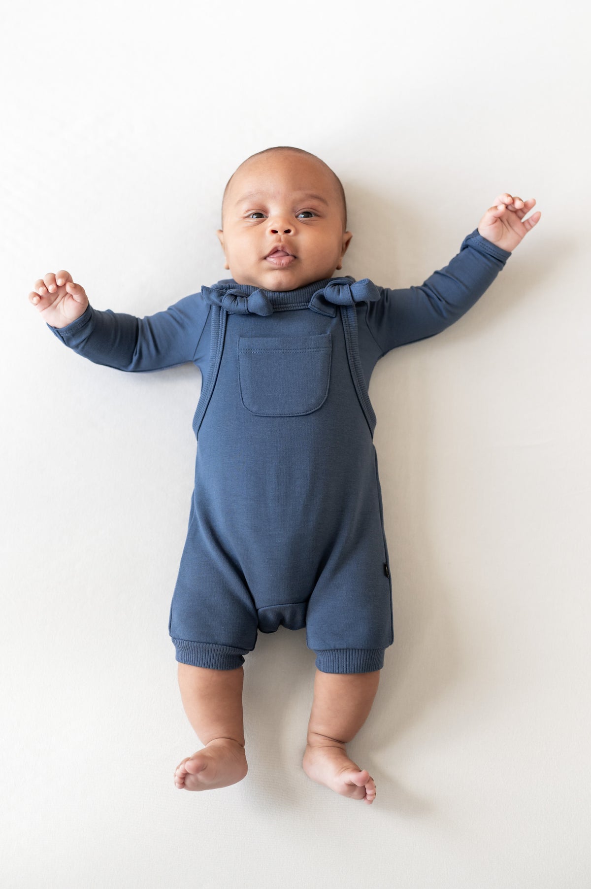 Baby wearing Overall in oxford color over similar color shirt on a beige background