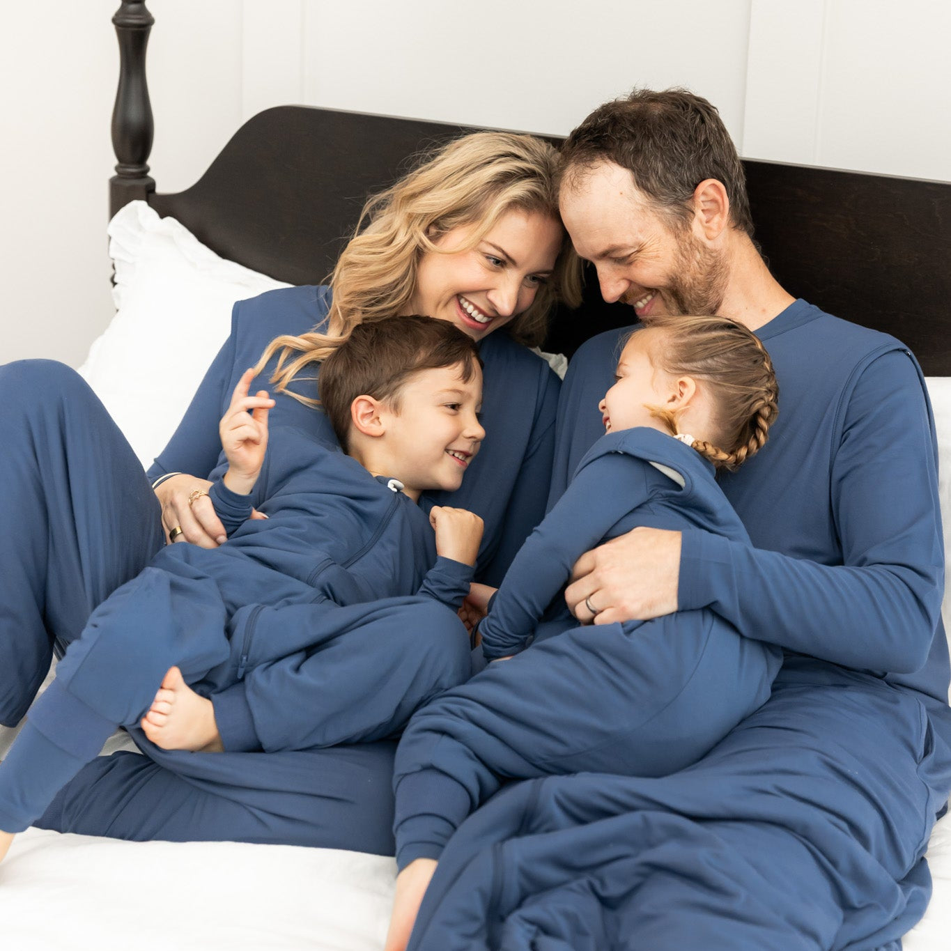 Family of snuggled in bed wearing matching sleep bag walkers in a dark blue color