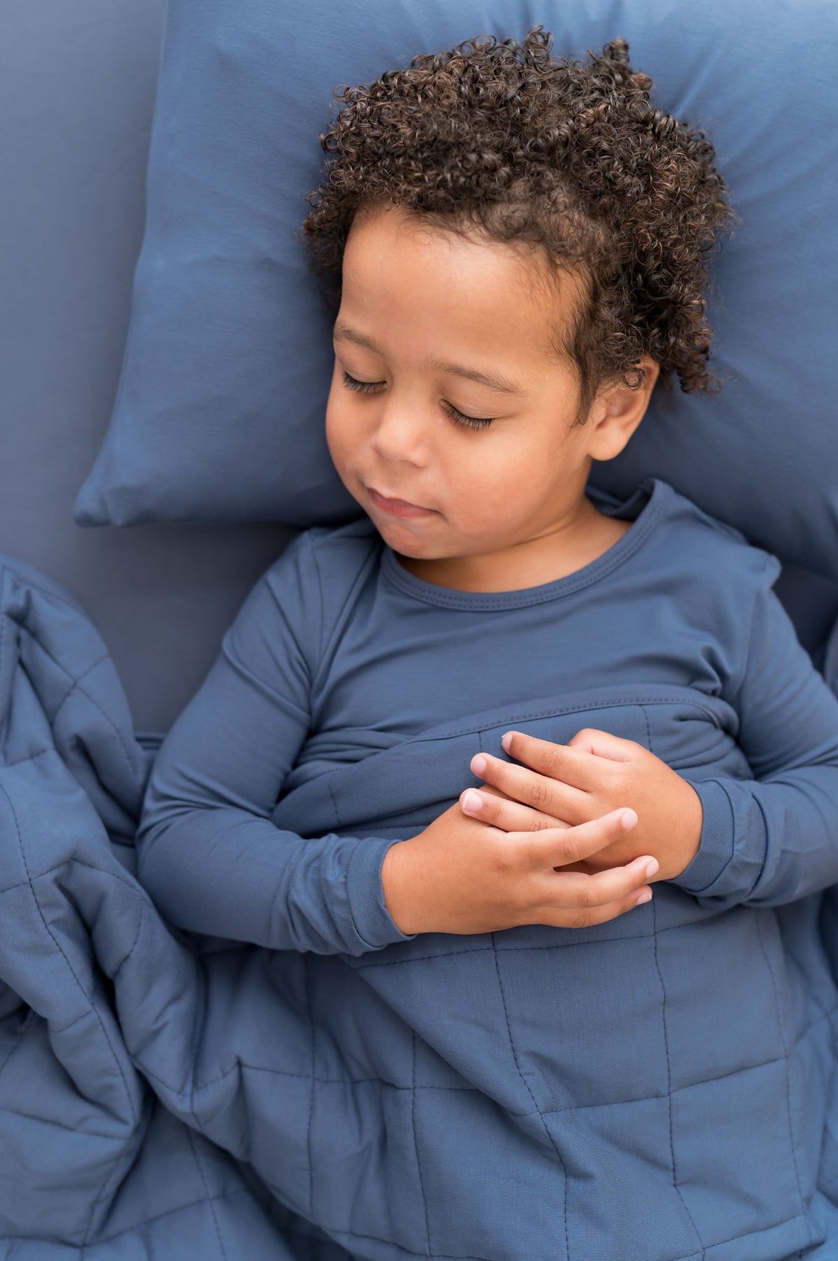 Boy sleeping on Toddler Pillowcase and sheet in Oxford covered under similar color blanket and wearing Oxford shirt