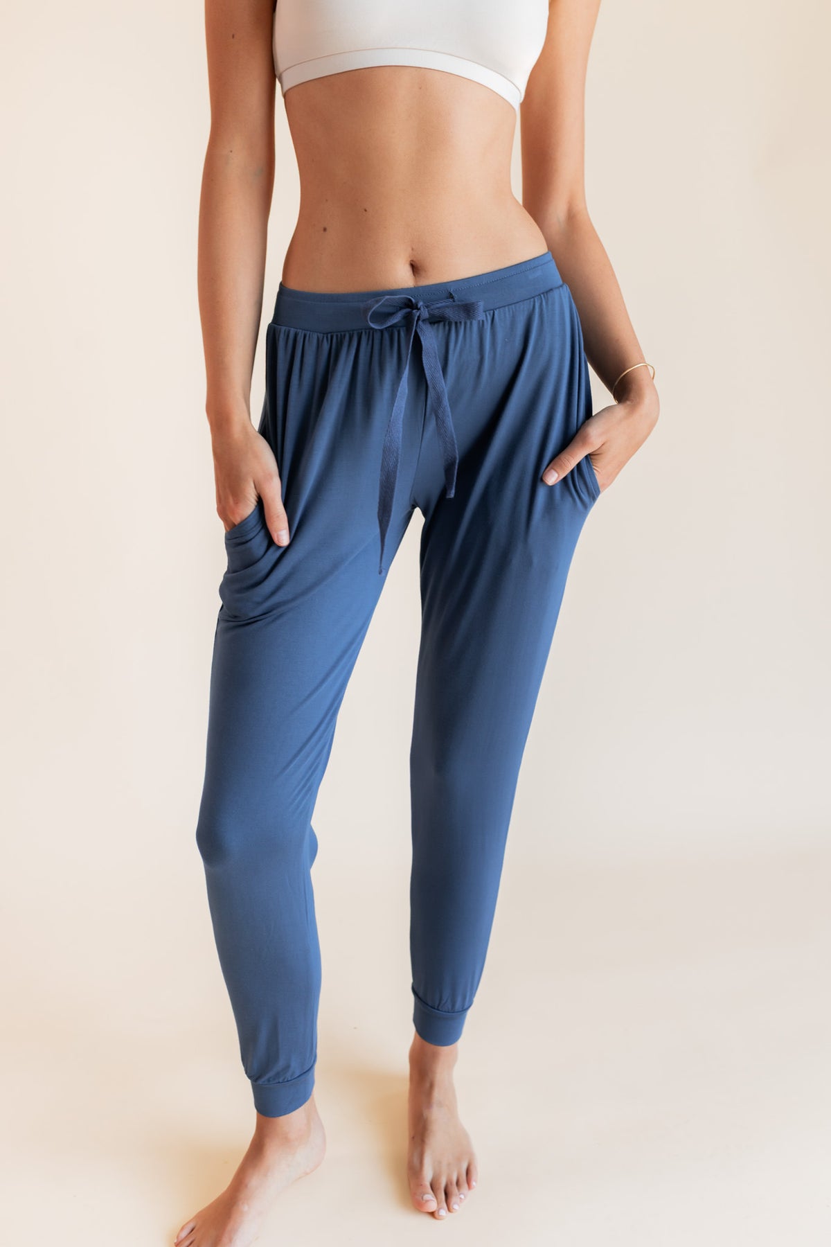 Model wearing Women's Jogger Pants in Oxford with pockets under a white bralette top on a beige background