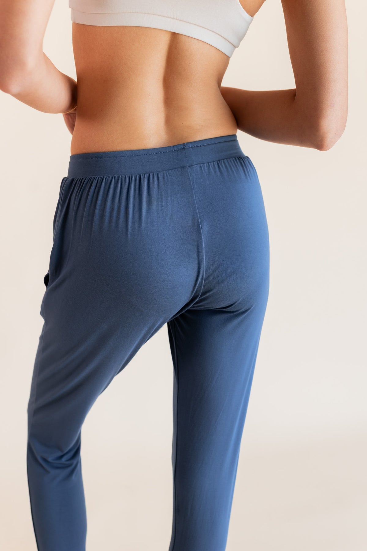 Back side of Model wearing Women's Jogger Pants in Oxford under a white bralette top on a beige background