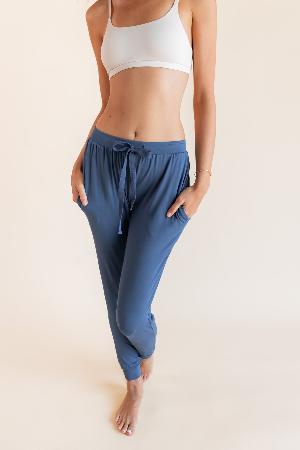 Close up of Model wearing Women's Jogger Pants in Oxford with pockets under a white bralette top on a beige background