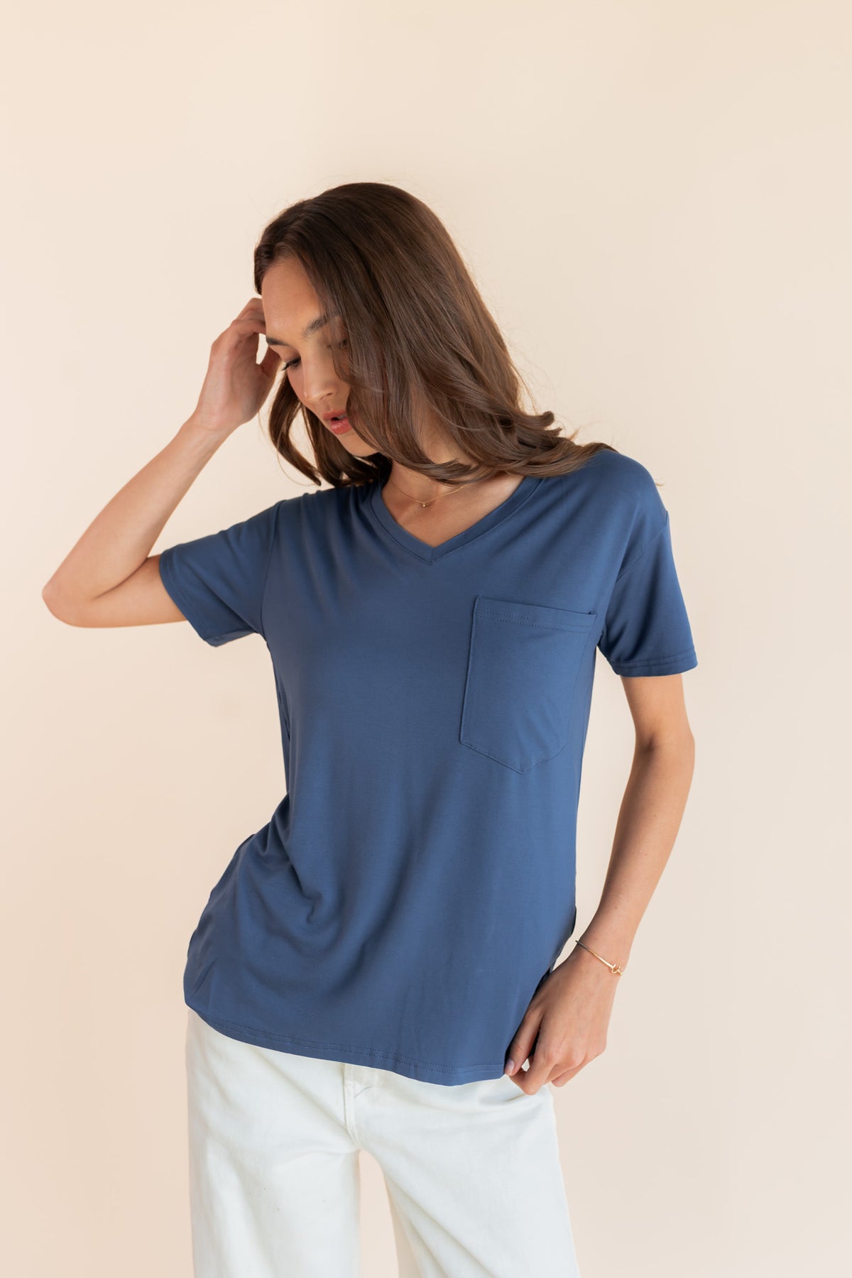 Model posing in Women's Oversized V-Neck Tee in Oxford over white pants on a beige background