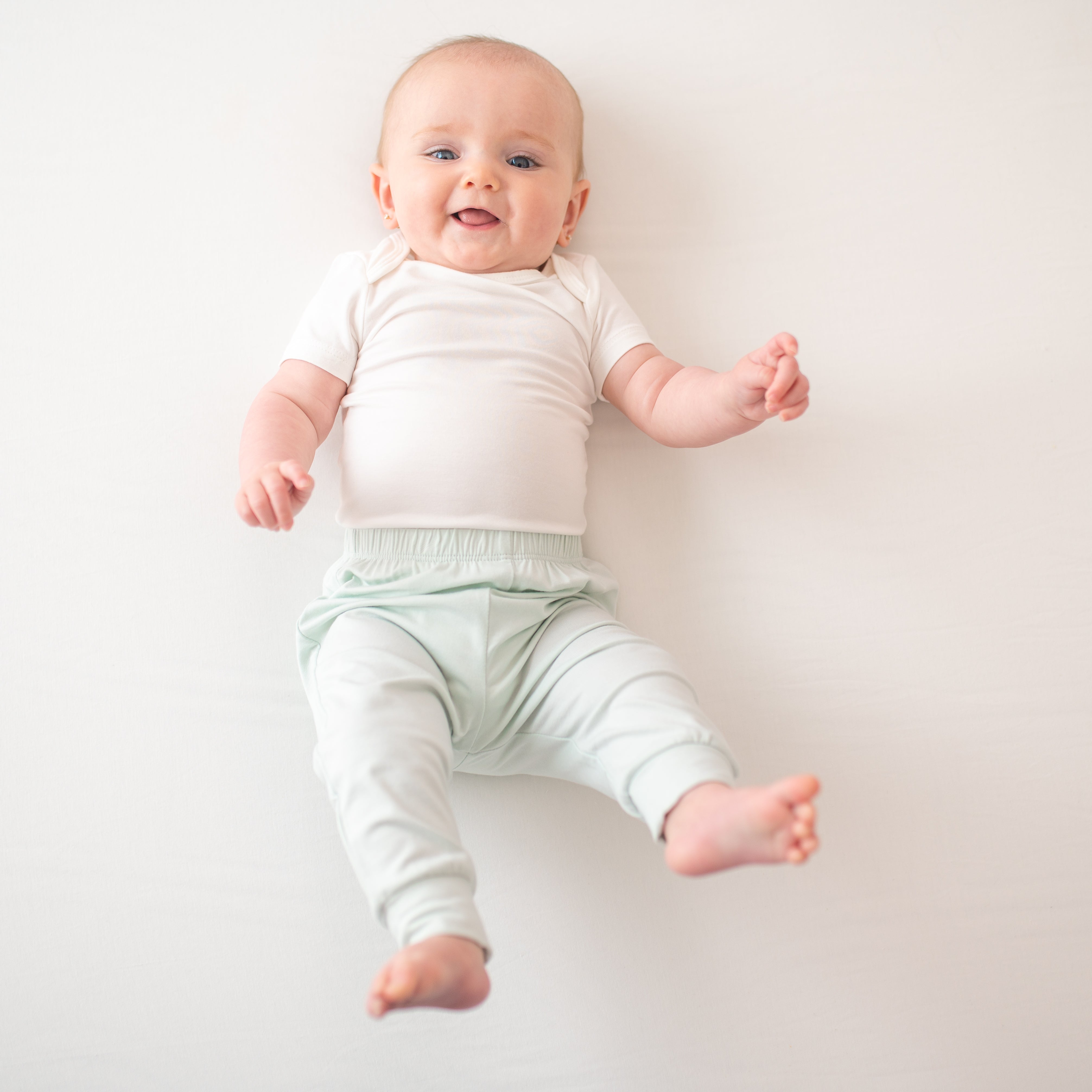 Infant model with legs up in the air wearing the Pant in Dew paired with a Cloud Bodysuit