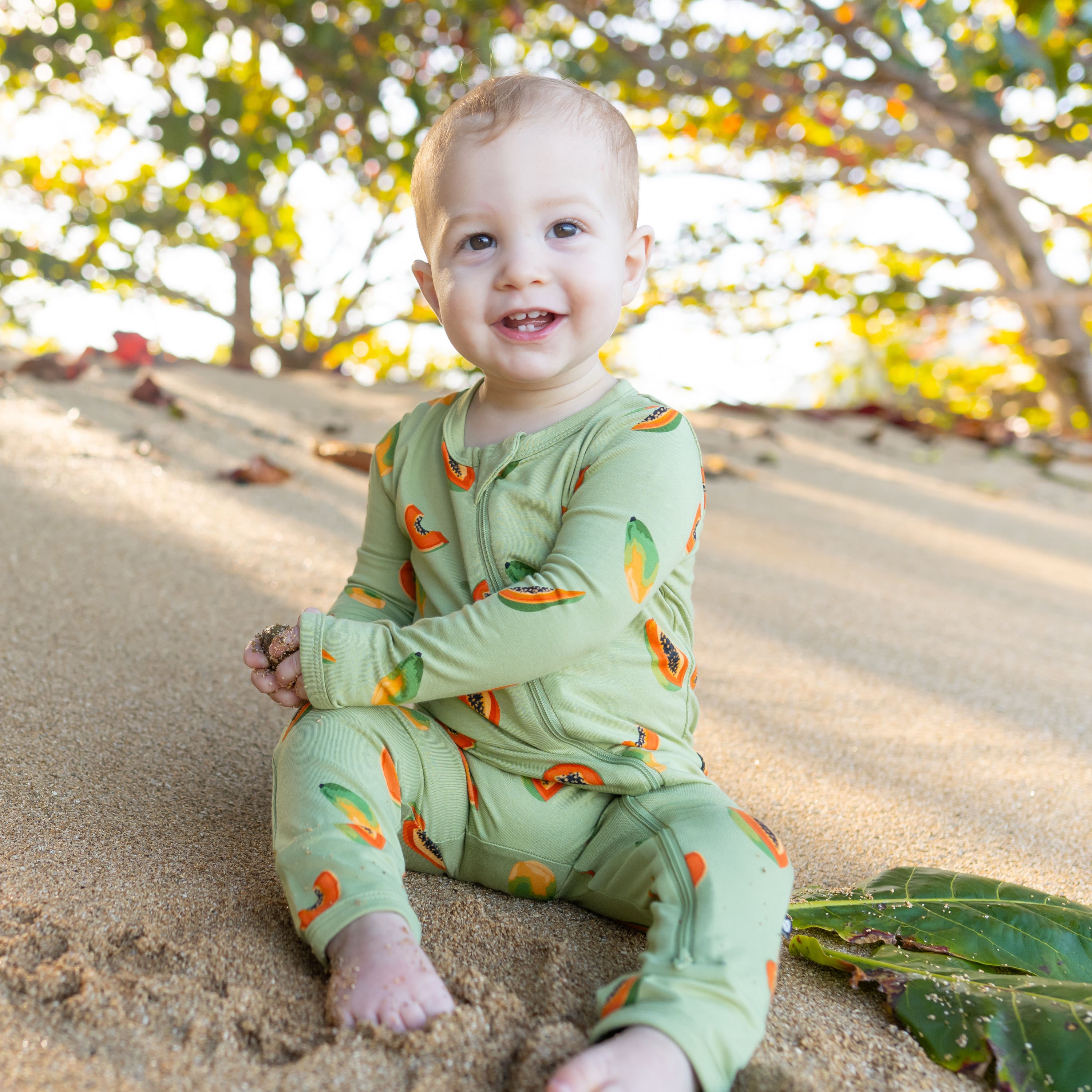 Baby sitting on beach wearing Papaya Zippered Romper