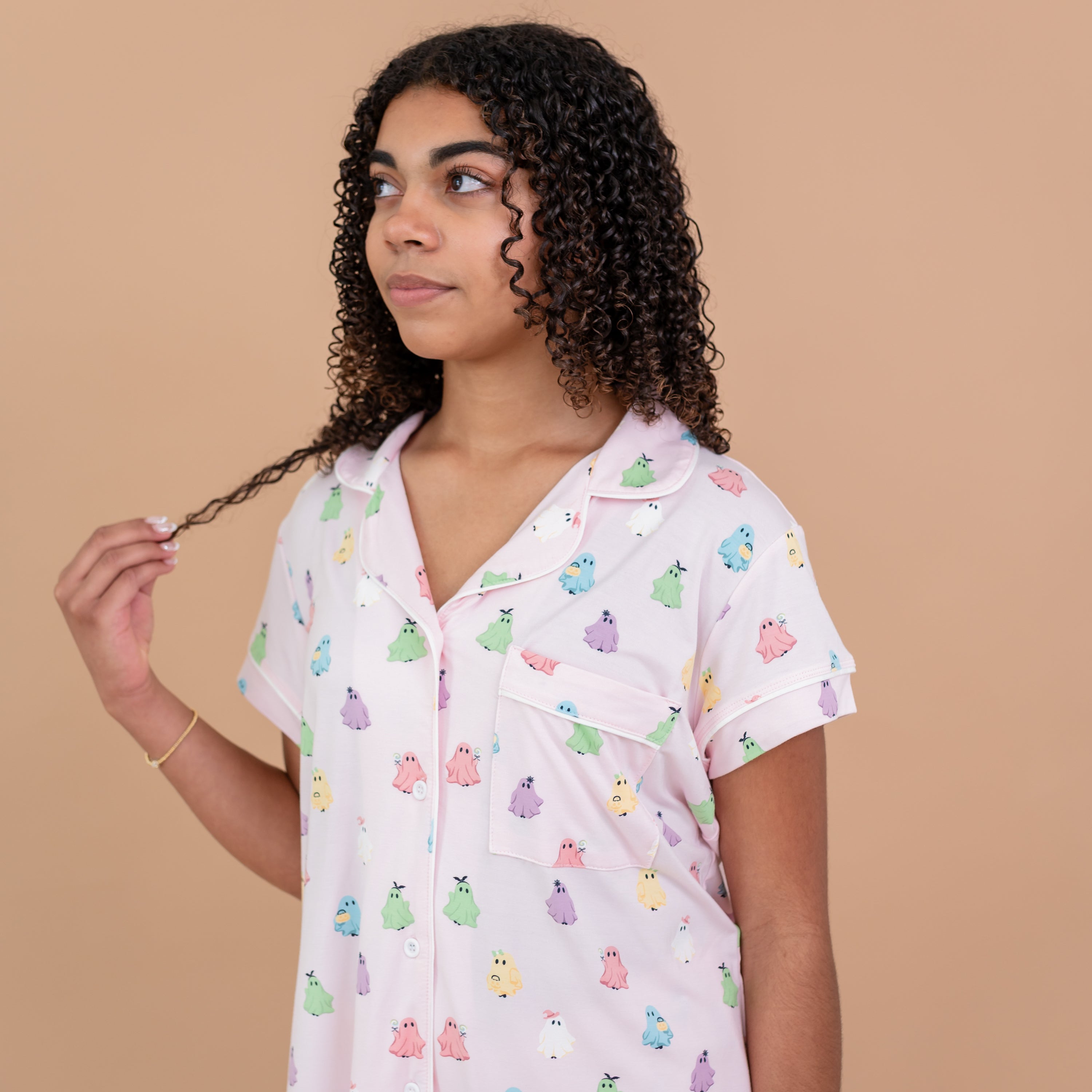 Close up photo of a model holding the ends of her hair looking off to the side wearing the Women's Short Sleeve Pajama Set in Pastel Ghost. Focus on the Cloud Trim and chest pocket