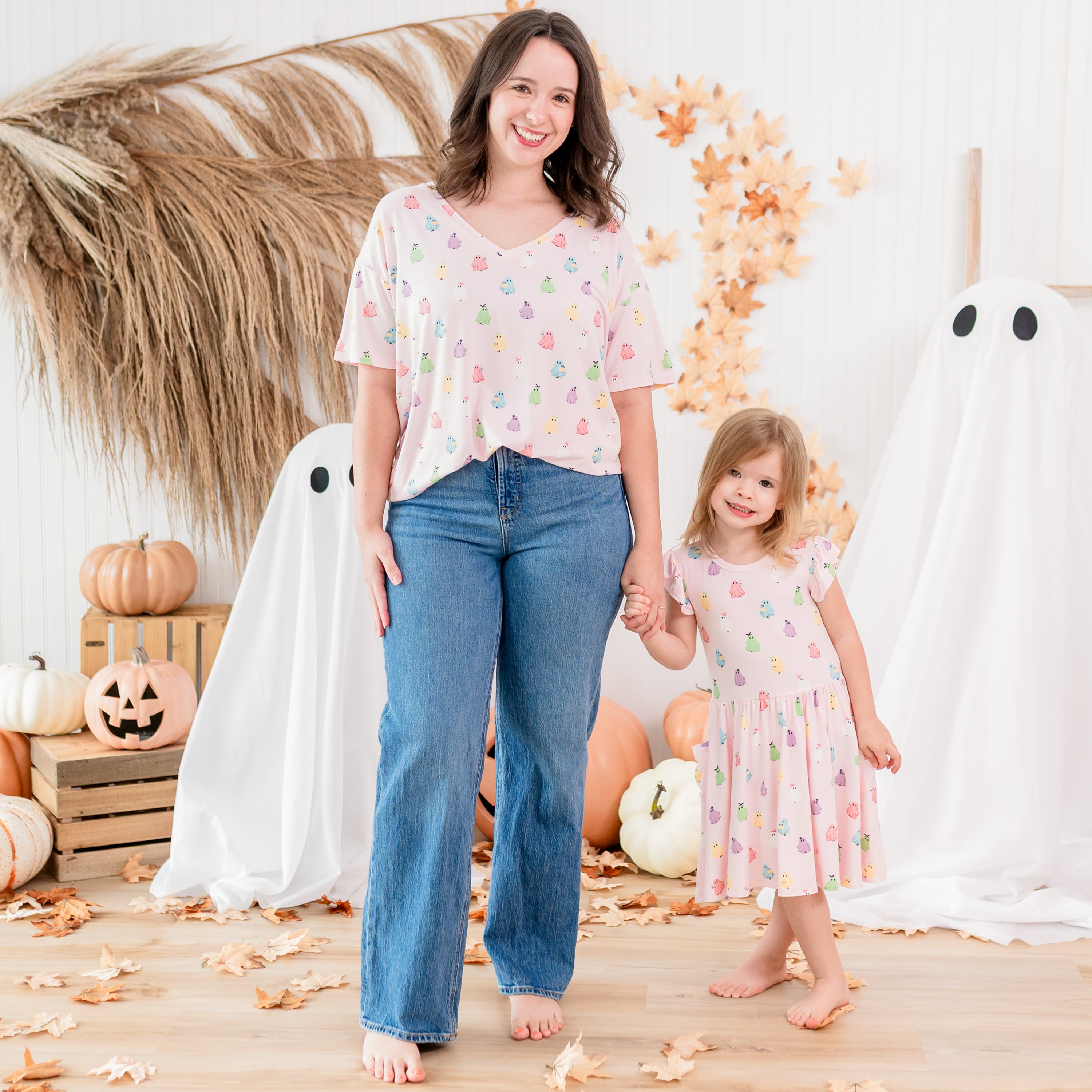 Mother and daughter matching in Pastel Ghosts standing in front of a fall backdrop. Mother wearing the Women's relaxed V-neck is holding the hand of her daughter wearing the Pocket dress