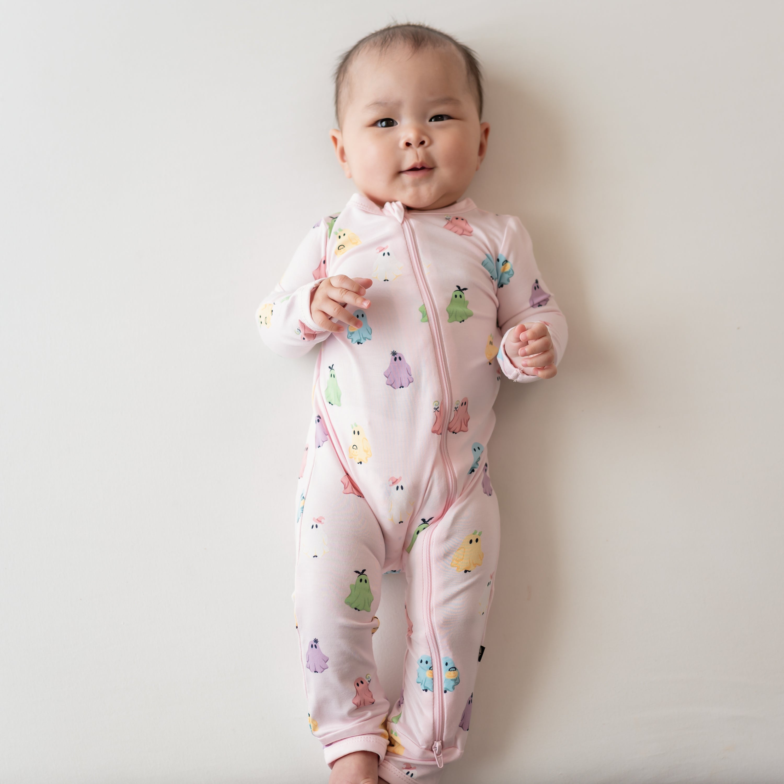 Infant laying on a light colored background wearing the Zippered Romper in Pastel Ghost