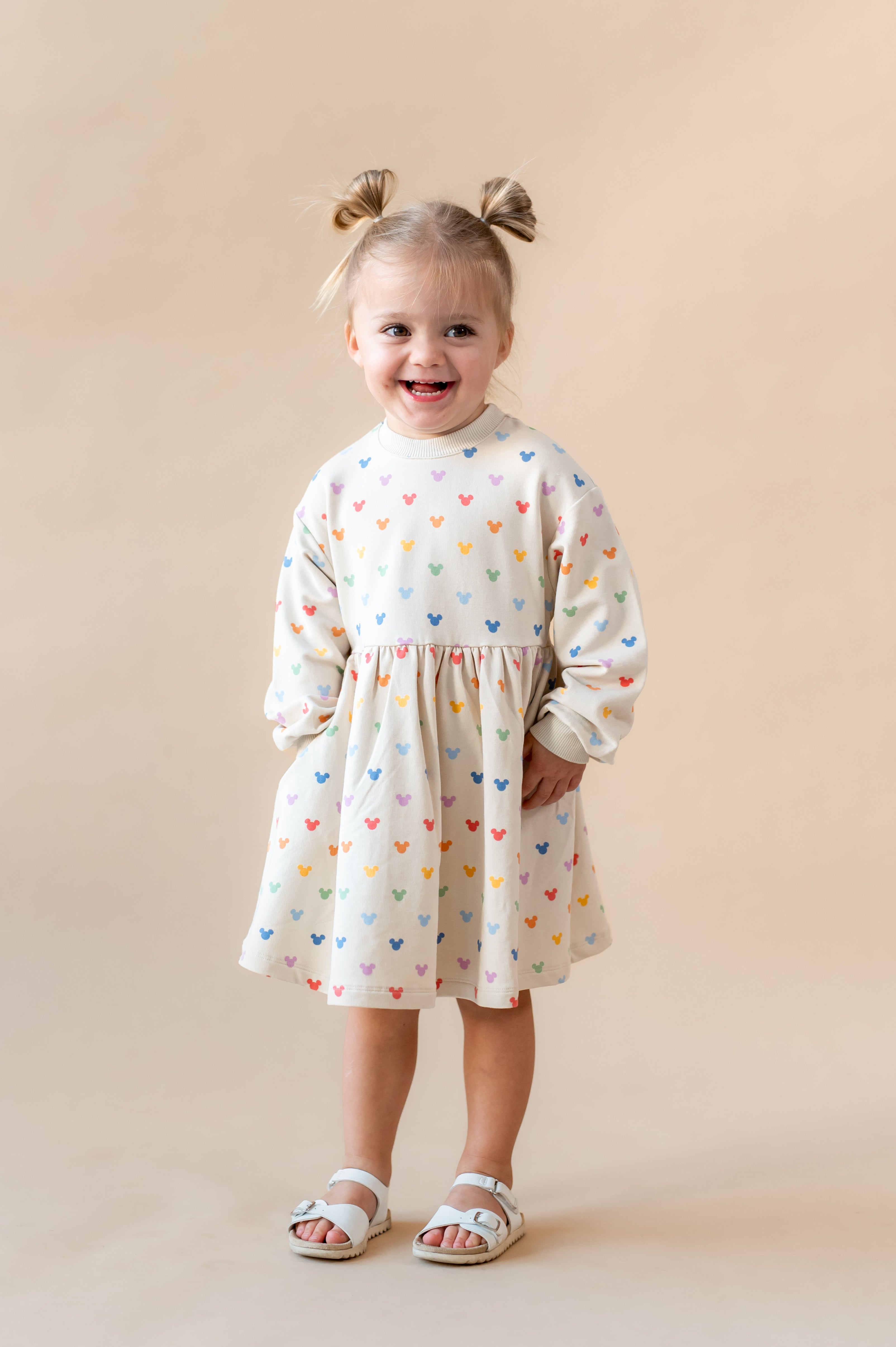 Girl smiling with her hands in her pocket wearing pastel mickey dress.