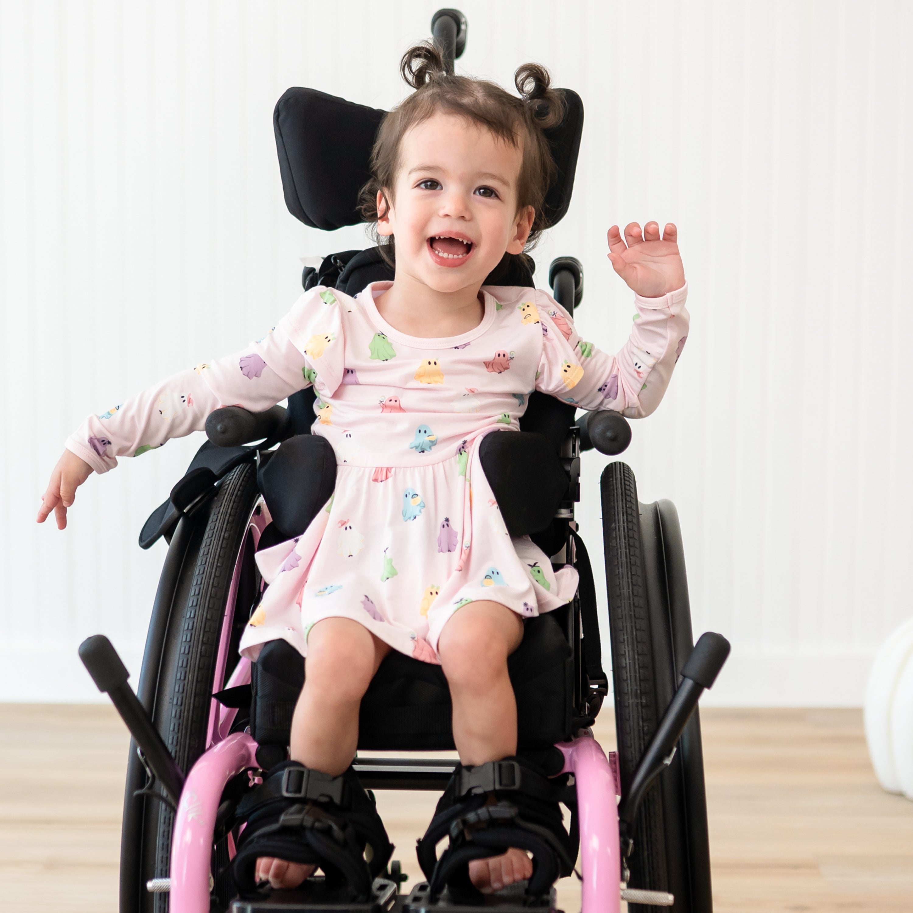 Smiling young girl sitting in her wheelchair wearing the Long Sleeve Twirl Bodysuit Dress in Pastel Ghost