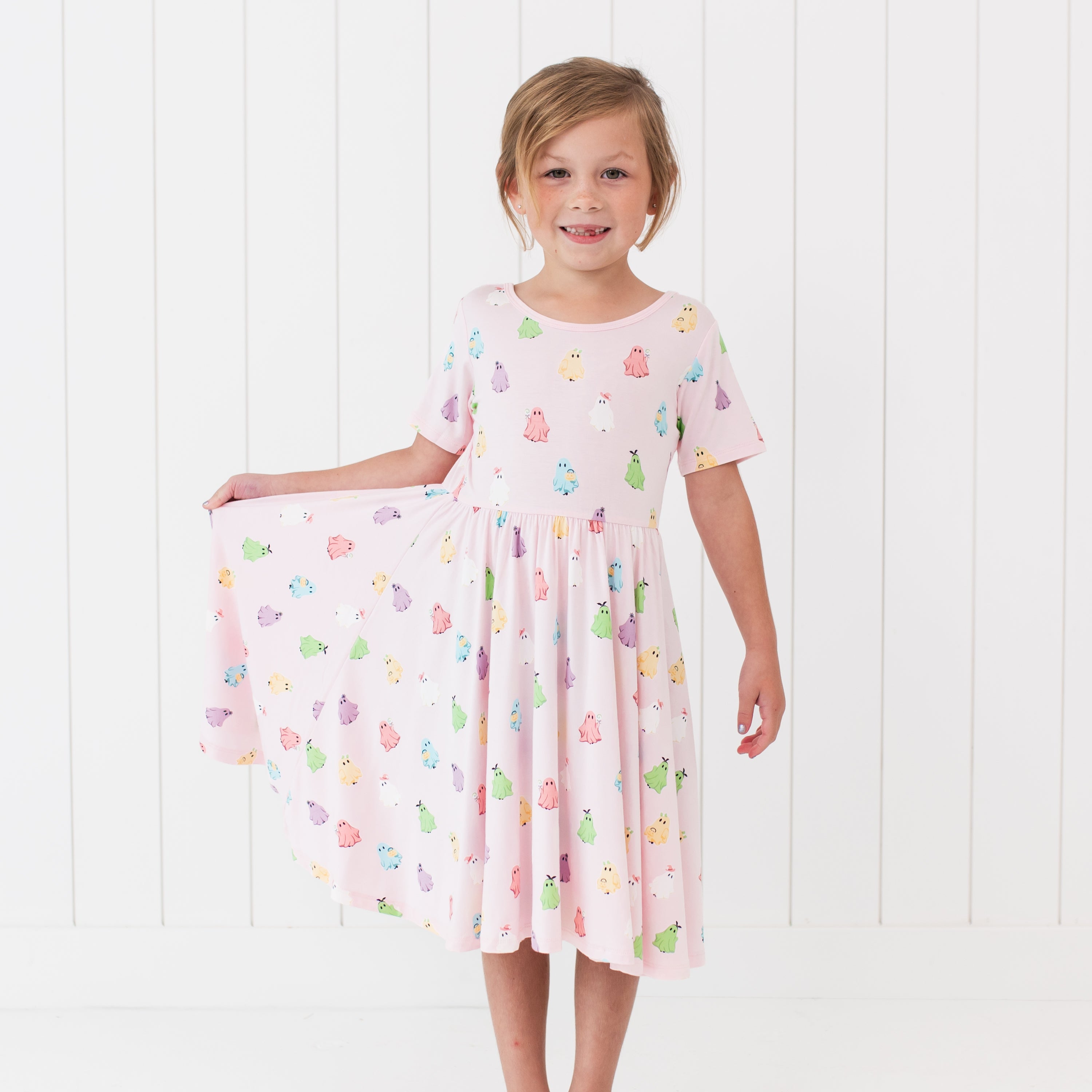 Young girl wearing a pink dress with colorful ghosts against a white background