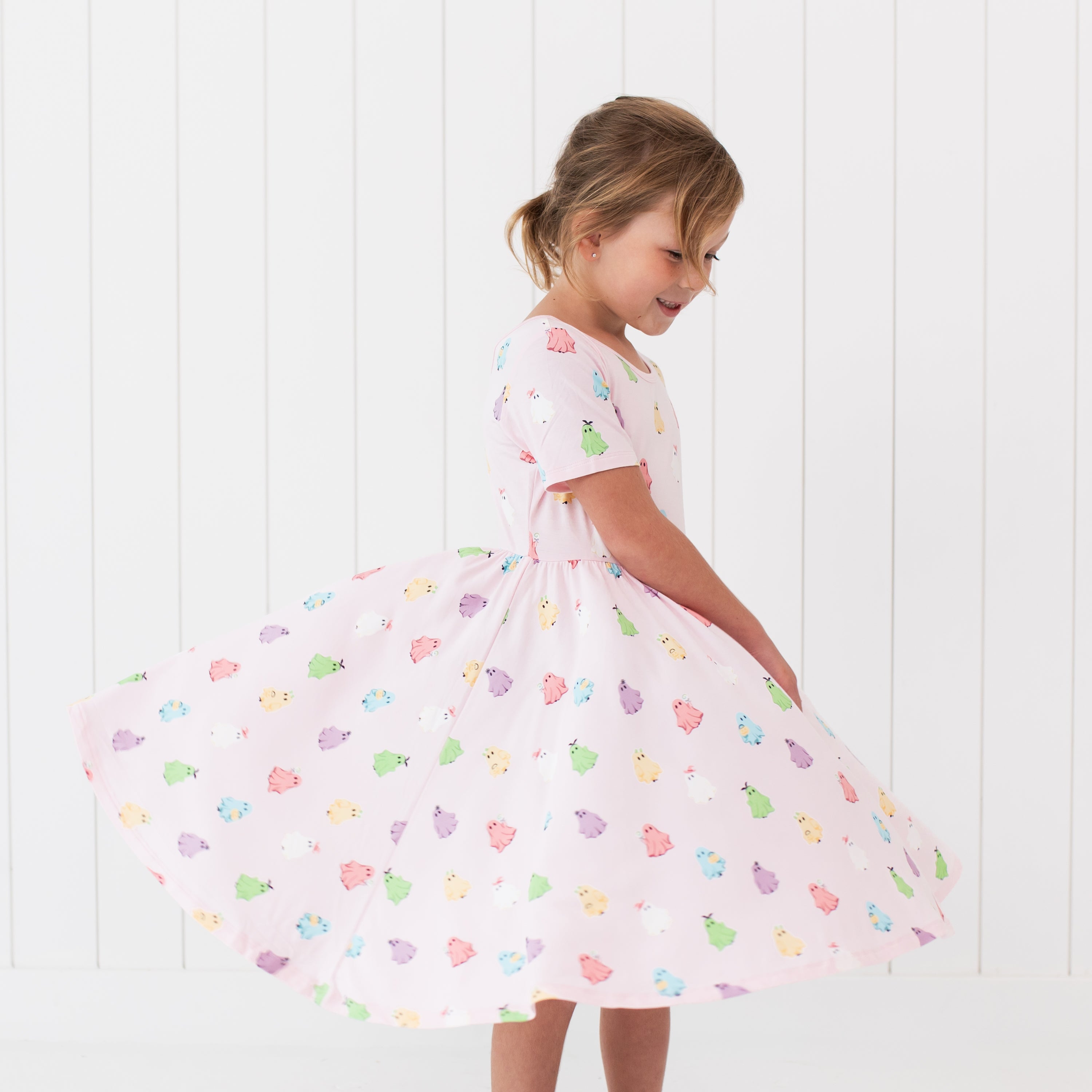 Young girl wearing a light pink dress with colorful ghost pattern against a white background